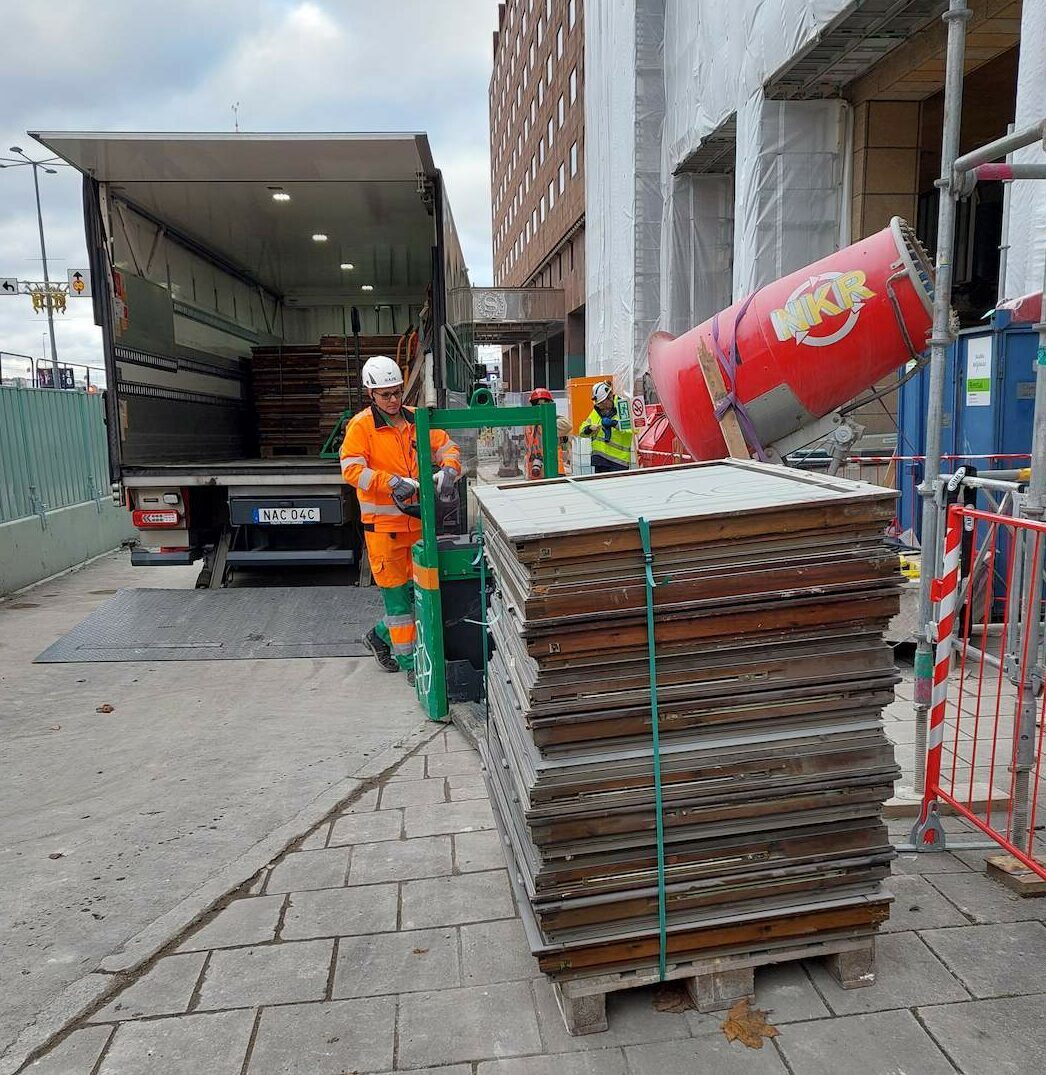 Byggarbetsplats där arbetare lastar av fönster från en lastbil med hjälp av lyftutrustning.
