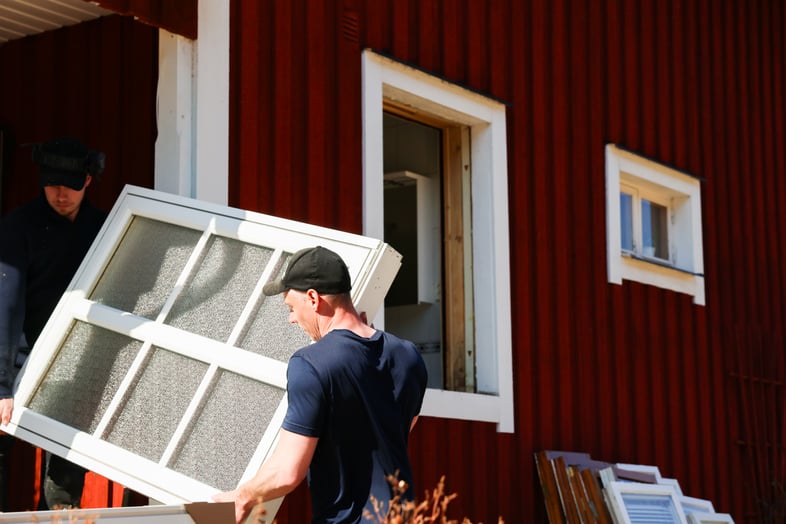 Två män bär in ett fönster i ett rött hus