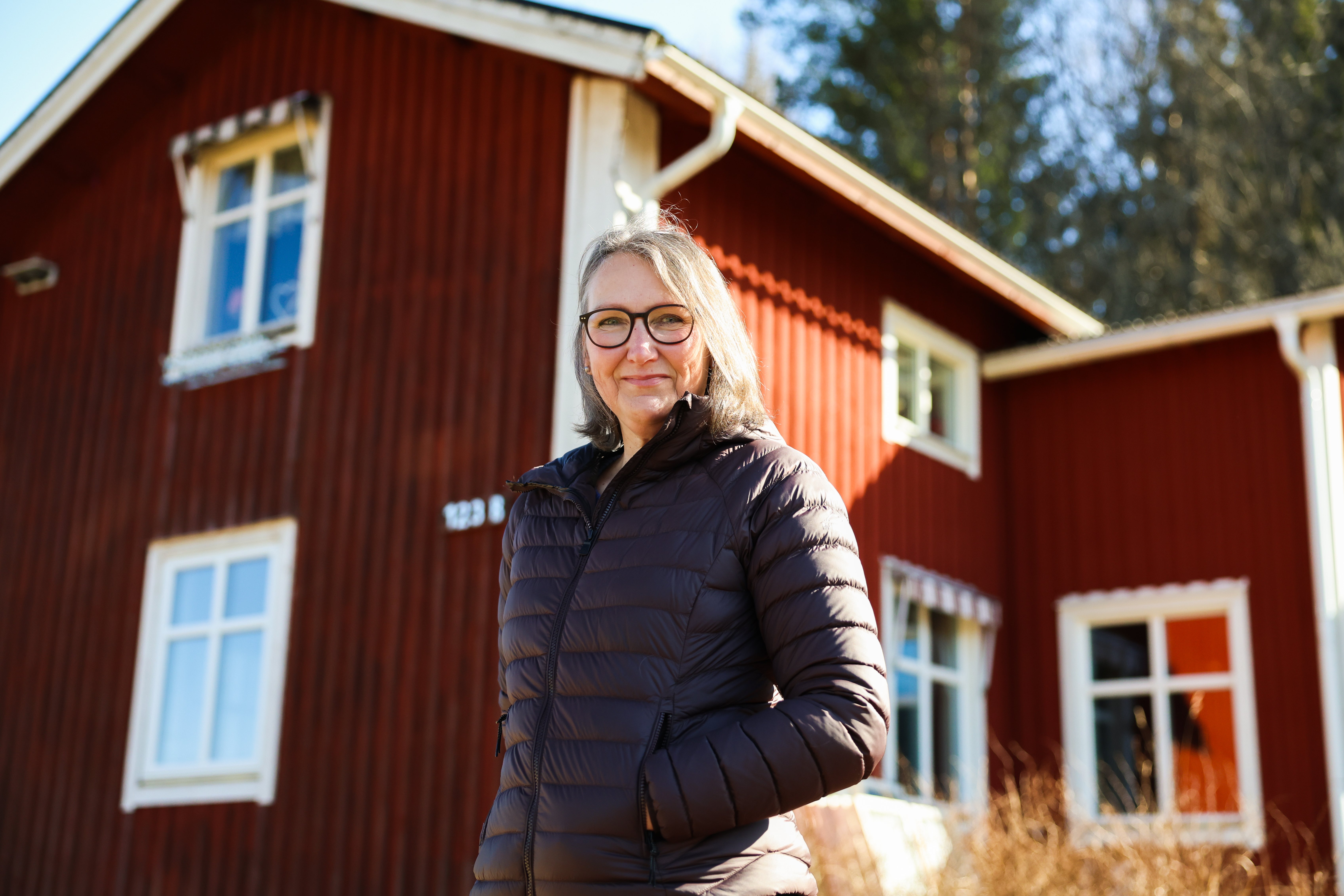 Kvinna i svart dunjacka står framför ett rött hus med vita knutar