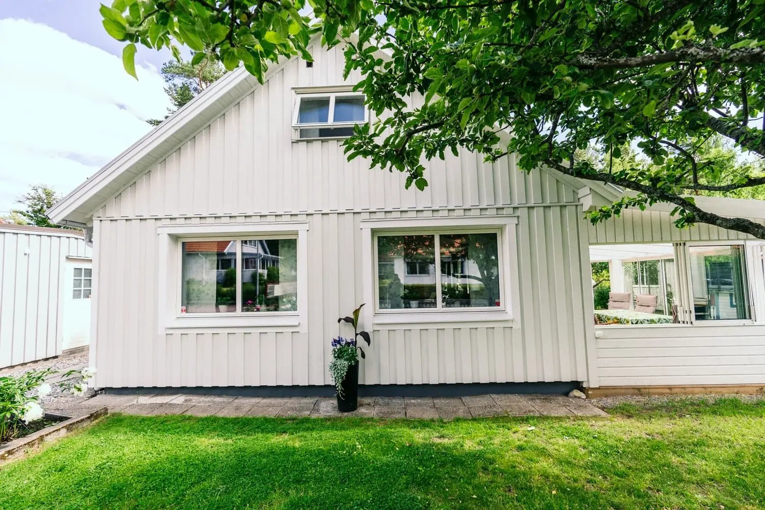 Baksida av ljusgrå villa i Falun med nya vita Prima-fönster från Mockfjärds, grönskande trädgård och inglasad altan till höger.