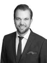 Porträt von Patrik Broin, der in Anzug und Krawatte vor einem hellen Hintergrund lächelt.