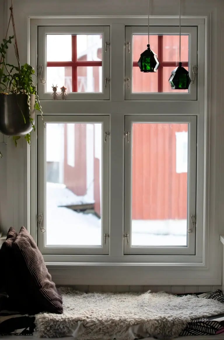 Vitt sidohängt 3-glasfönster med fyra öppningsbara bågar och klassiska fönsterhakar, med utsikt mot snöigt vinterlandskap och röd byggnad utanför.Sonnet 4.6
