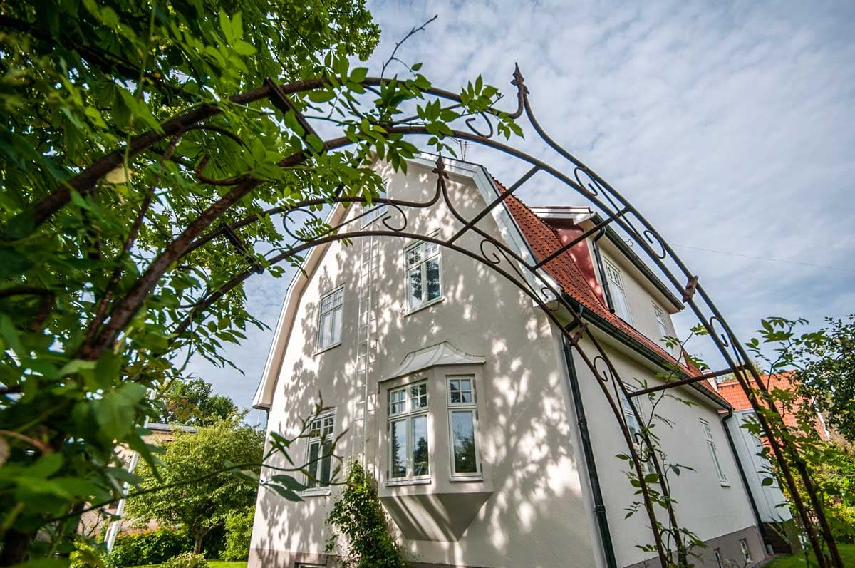 Vit villa med spröjsade fönster sedd genom en dekorativ trädgårdsportal.