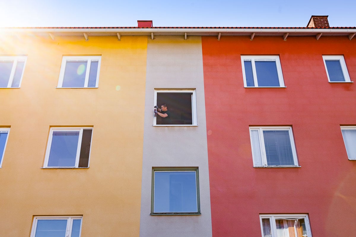 Person installerar fönster i flerfamiljshus med färgglad fasad.