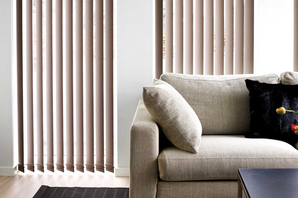 Vardagsrum med vertikala lamellgardiner och soffa vid fönster.