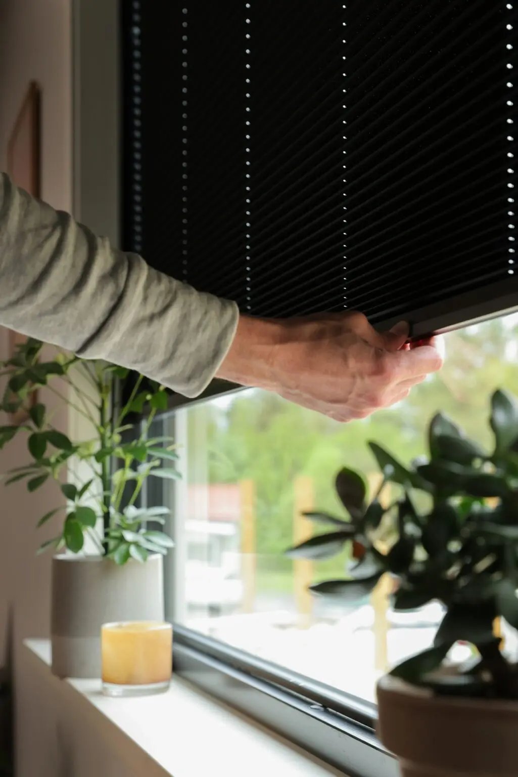 Hand som justerar en svart mellanglasskydd i ett svart aluminiumbeklätt träfönster från Mockfjärds – energieffektiv renovering vid sjön Liljan i Dalarna.