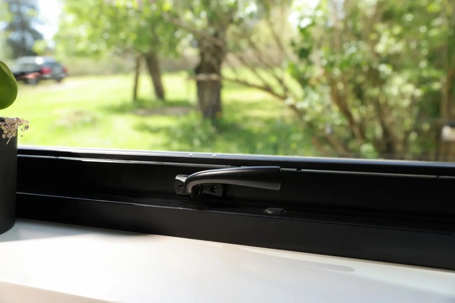 Närbild på svart handtag och spaltventil på ett aluminiumbeklätt vridfönster från Mockfjärds serie Ultimat – för naturlig ventilation utan att skada putsfasaden.