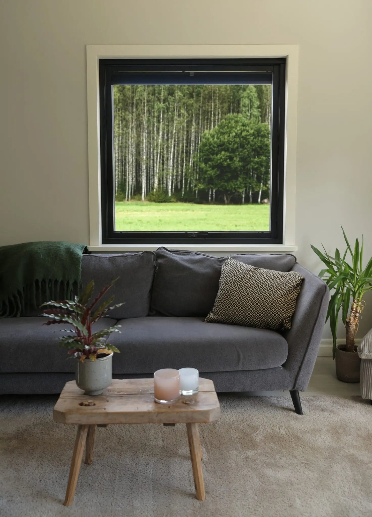 Vardagsrum med grå soffa och svart vridfönster utan mittpost från Mockfjärds serie Ultimat – stort ljusinsläpp med skogsutsikt i energieffektivt renoverat hus i Dalarna.