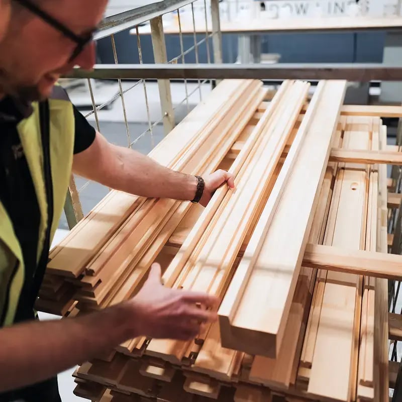 Person granskar och sorterar trädelar i en fabrik.