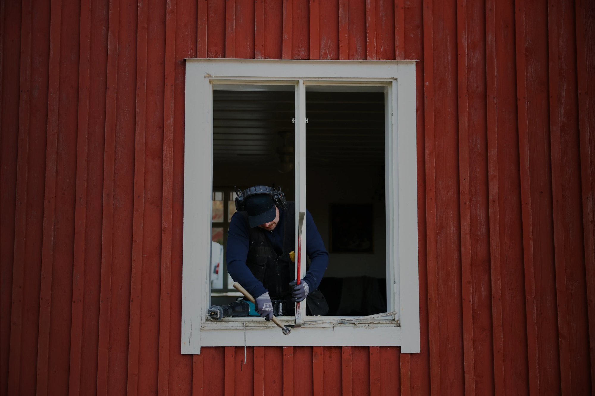 Man monterar ett nytt fönster i ett rött hus
