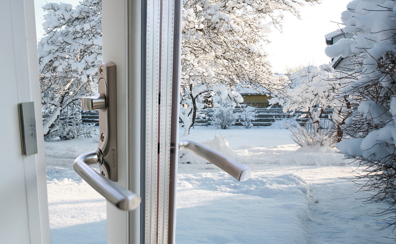Öppen altandörr med utsikt mot snötäckt trädgård.