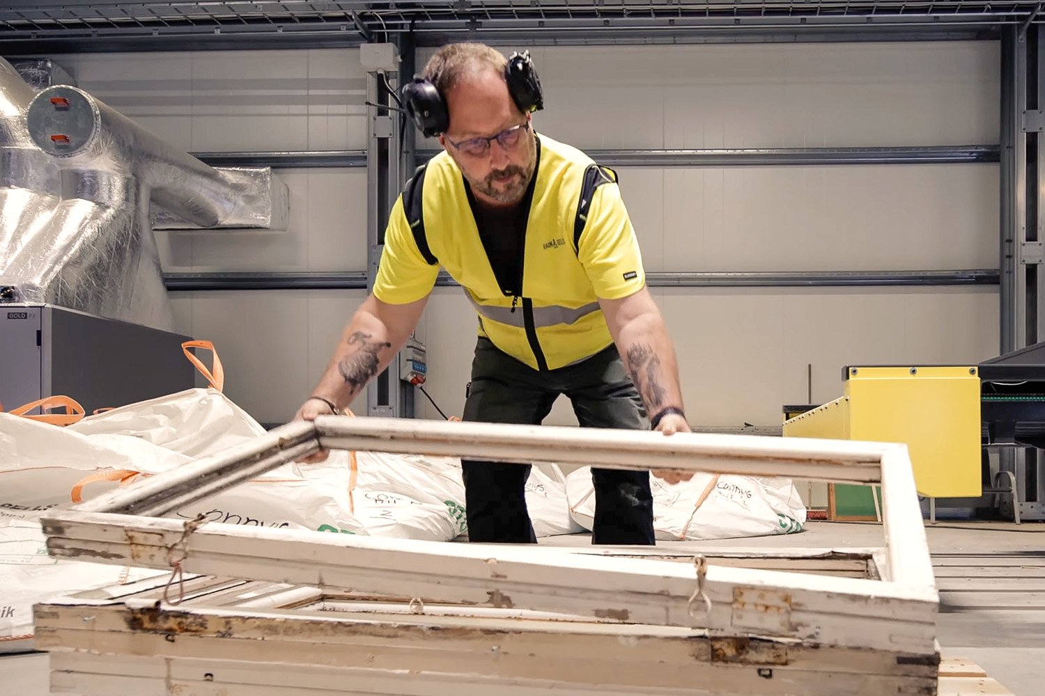 Arbetare demonterar gamla fönster för återvinning i industrimiljö.