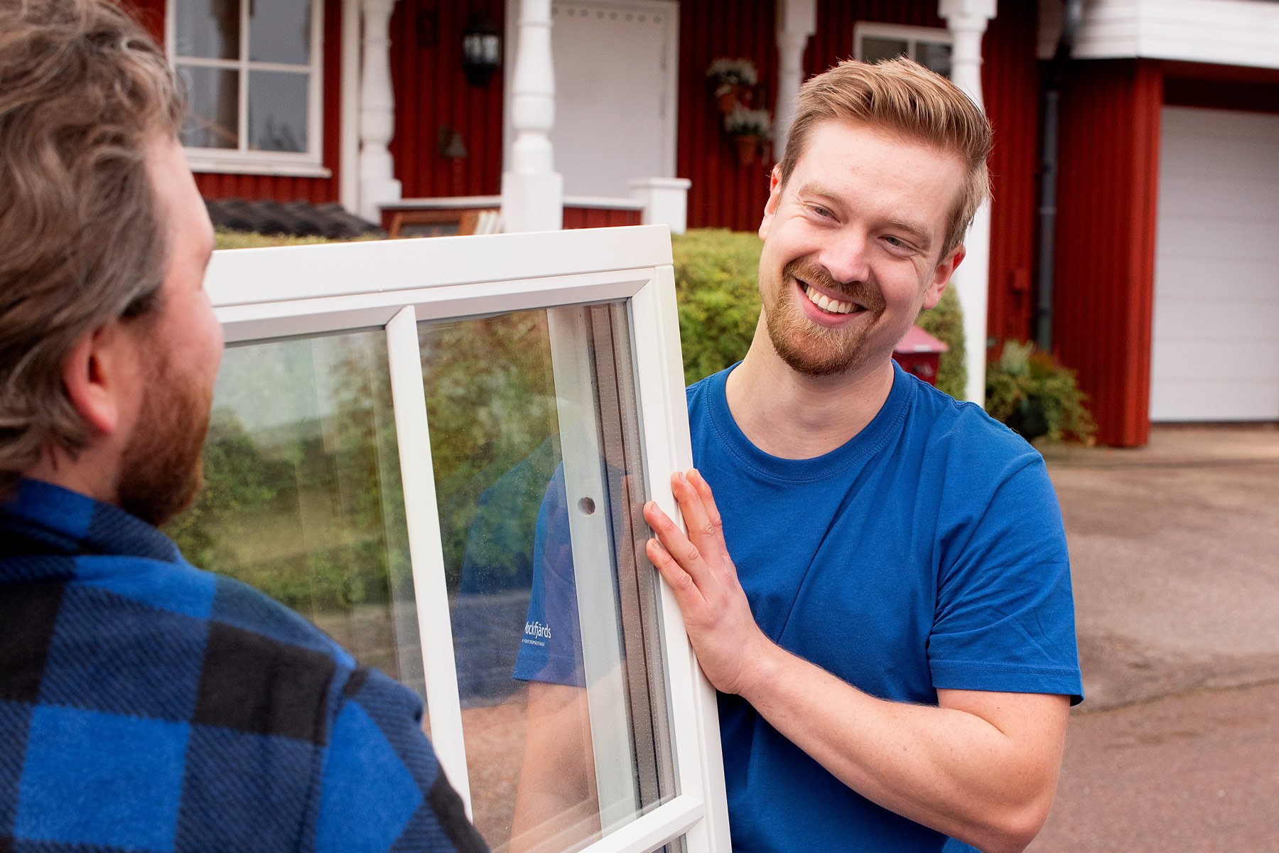 Leende man håller upp ett fönster utanför ett hus.