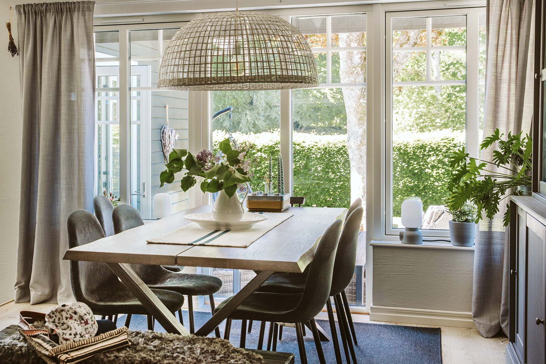 Ljust matrum med stora fönster, träbord och utsikt mot grön trädgård.