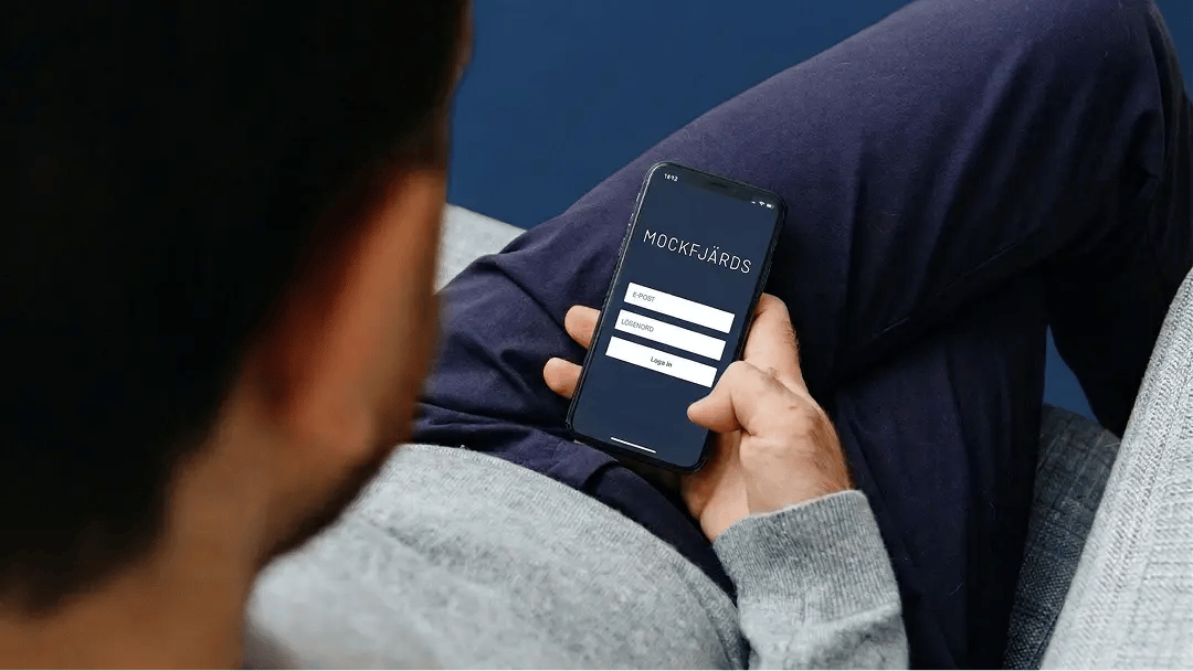 Person håller i mobiltelefon med inloggningssida för Mockfjärds.