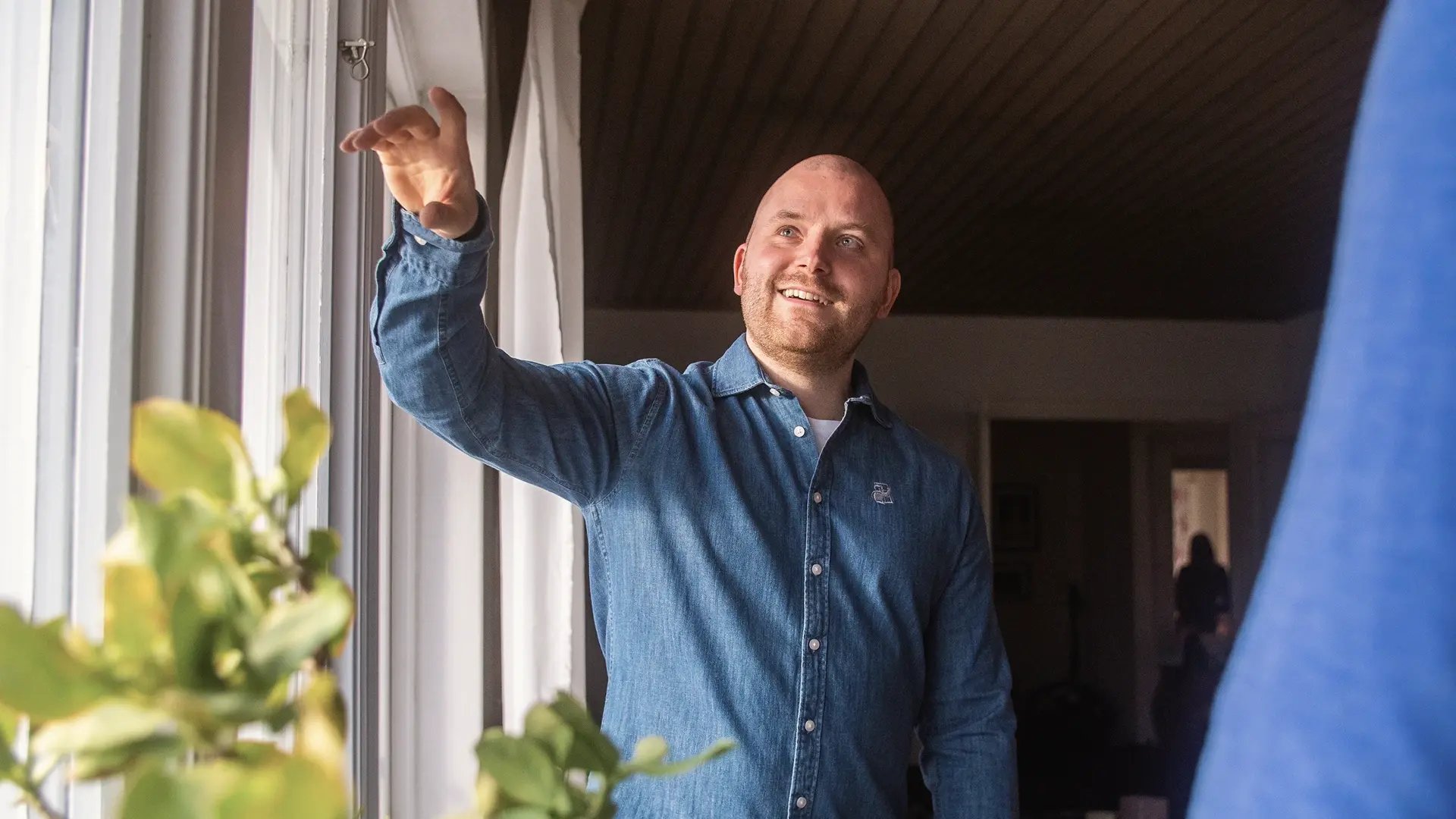 Man står vid ett fönster och pekar upp mot något medan han pratar.