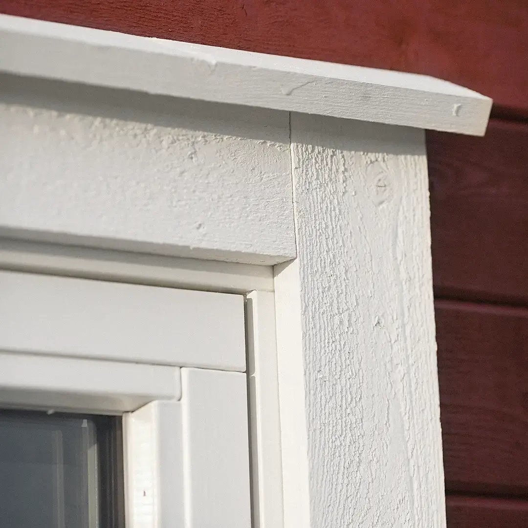 Detalj av ett vitt fönsterfoder på en röd träfasad