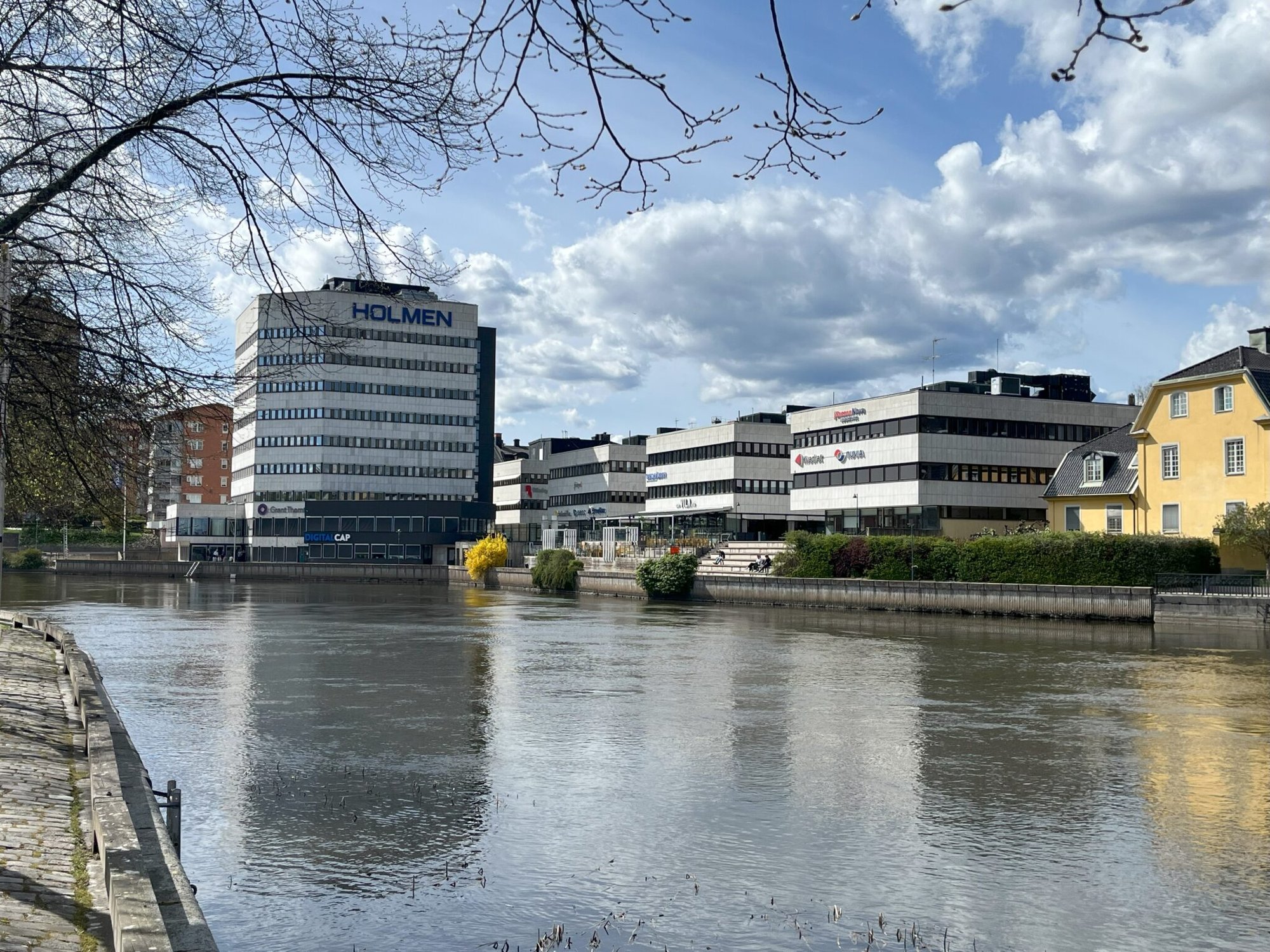 Holmenhuset och låghus på Bråddgatan i Norrköping speglade i Motala ström – fönsterbyte i flera etapper med Svanenmärkta fönster och återbruk av gamla fönster, utfört av Mockfjärds åt Lundbergs Fastigheter.Sonnet 4.6