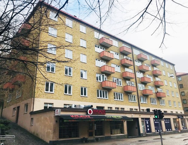 Exteriör av kulturhistorisk fastighet från 1938 med gul tegelfasad och röda balkonger – byte av 180 sidohängda inåtgående fönster med profilerad insida, utfört av Mockfjärds.