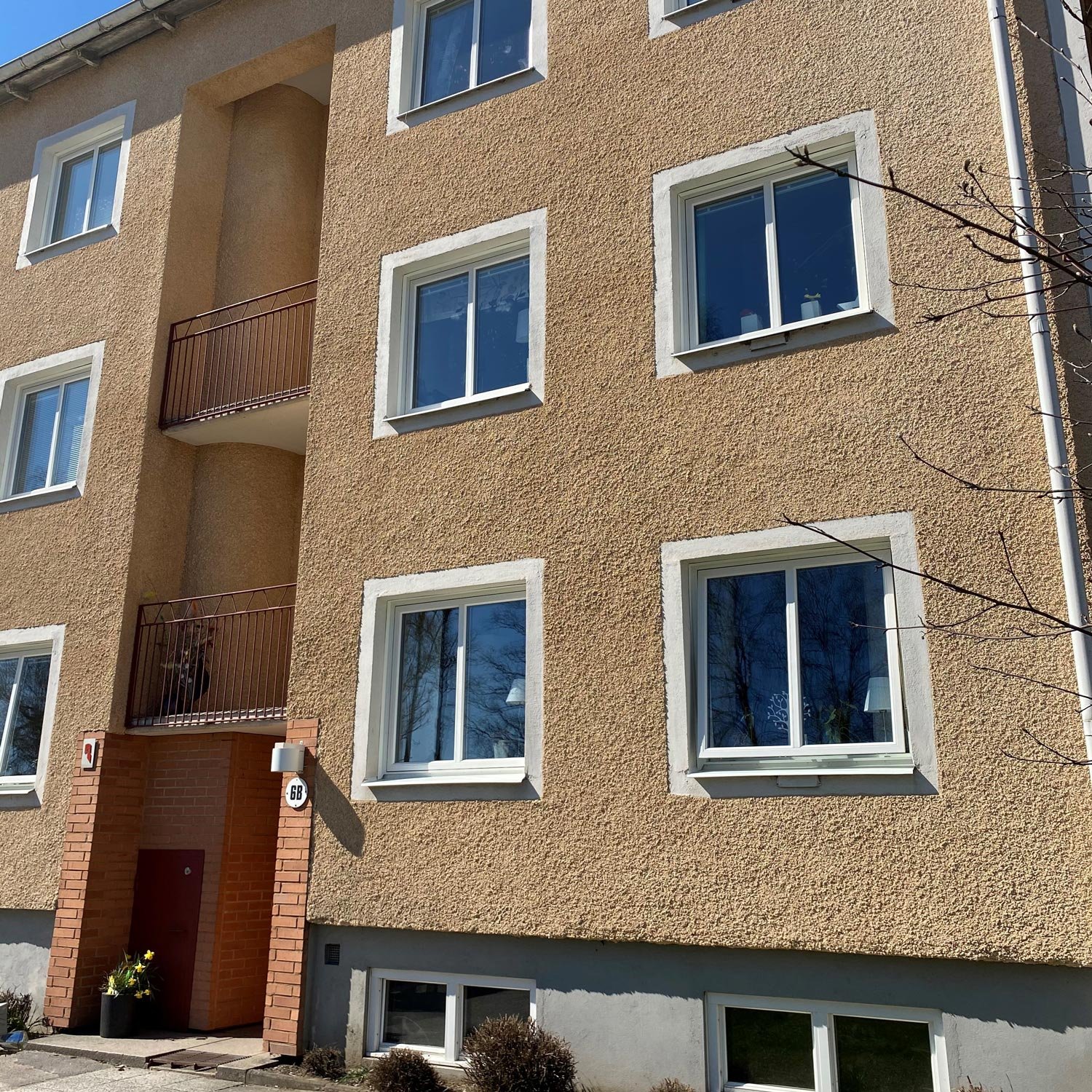 Närbild på nybytta vridfönster med vita karmar och genomgående mittpost på beige putsfasad – fönsterbyte med solskyddsglas och persienner i alla fönster, utfört av Mockfjärds.