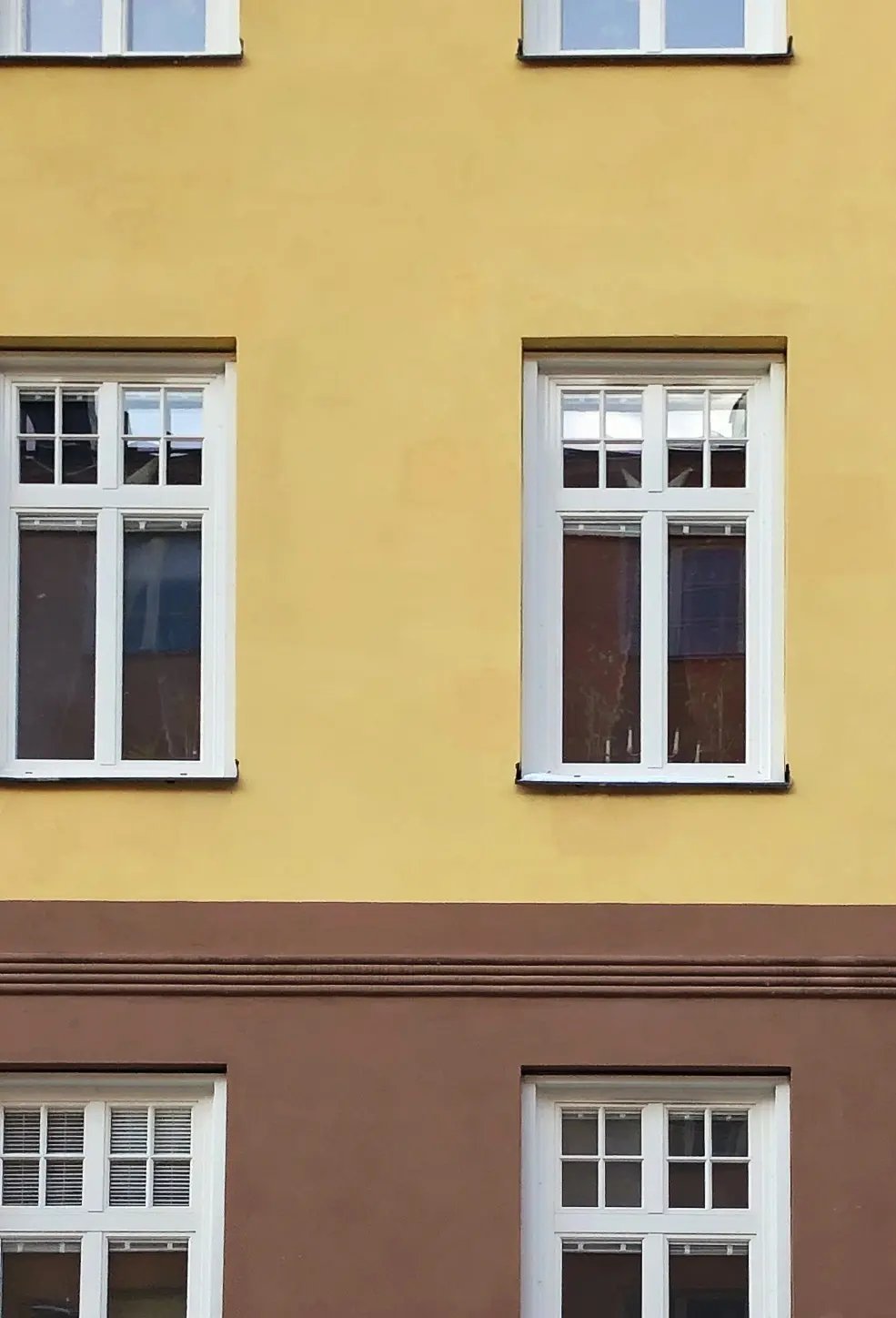 Närbild på nybytta spröjsade fönster med vita karmar på gul och brun putsfasad – fönsterbyte i BRF Bonden 29, centrala Södermalm.