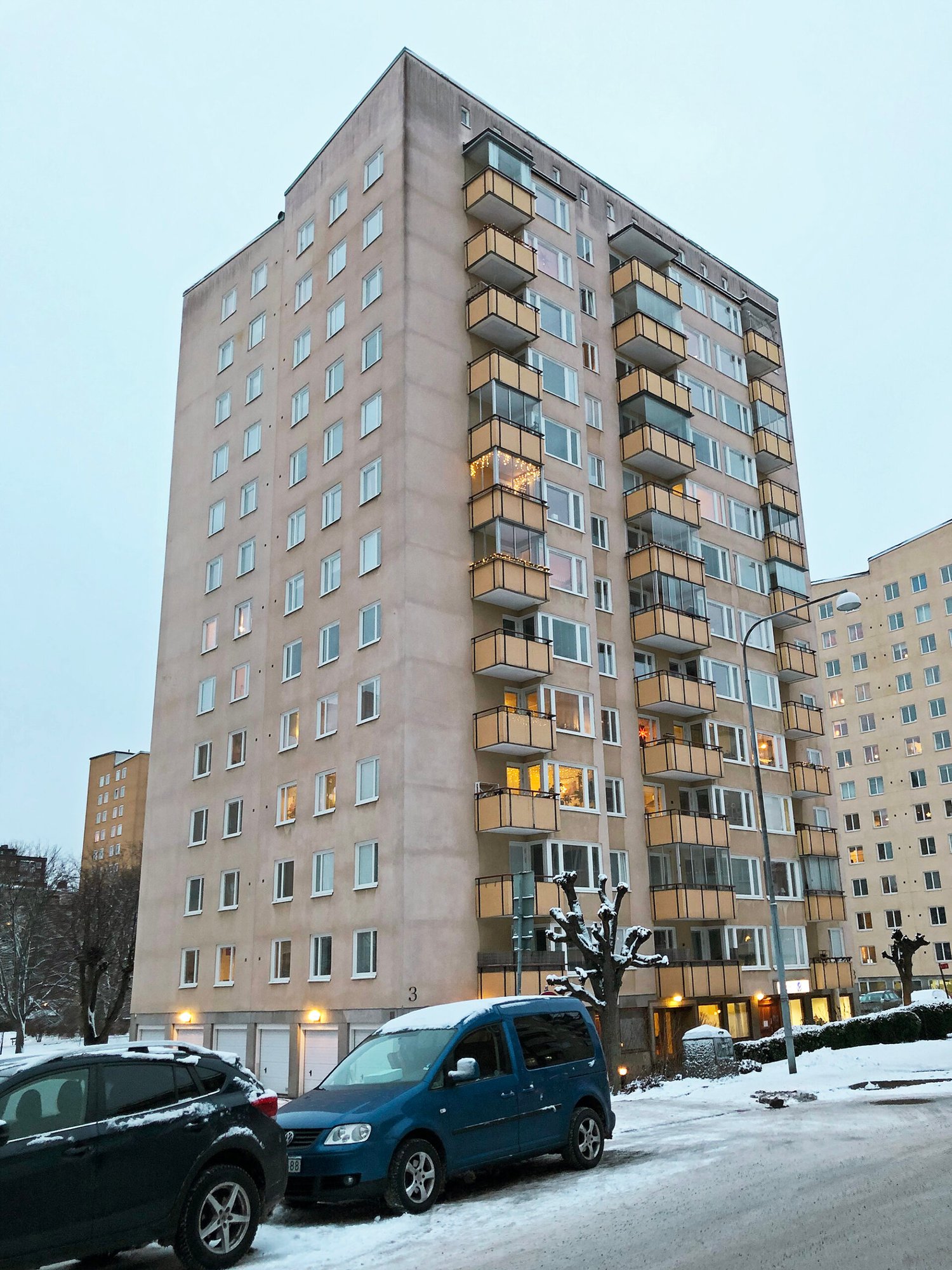 Exteriör av höghus med ljus putsfasad och inglasade balkonger – byte av ca 400 fönster med vita karmar utfört av Mockfjärds.