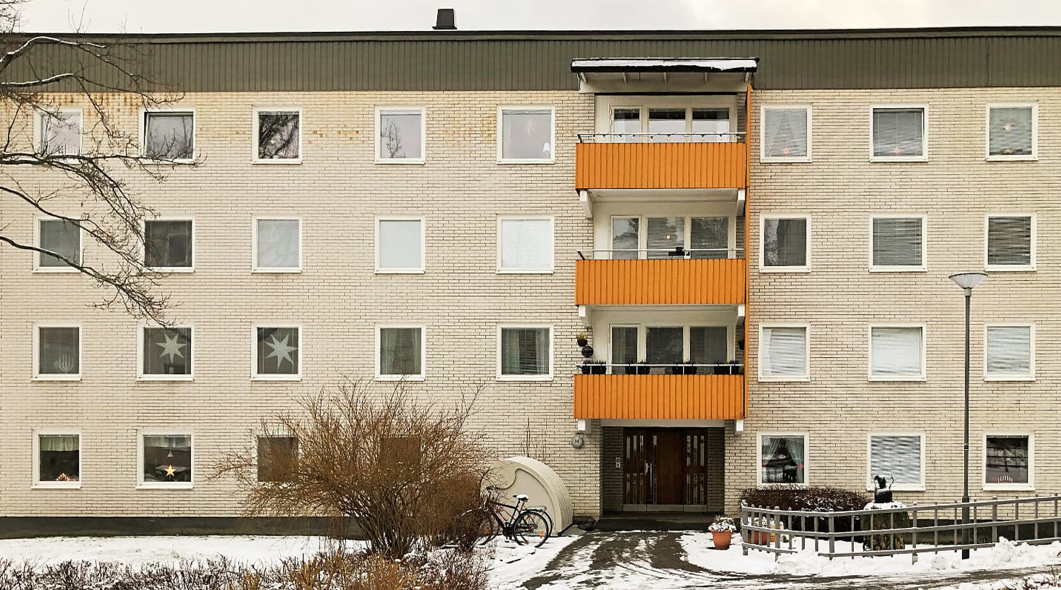 Exteriör av flervåningshus med ljus tegelfasad och orange balkonger – del av storskaligt fönsterbyte av ca 1300 fönster med vita karmar utfört av Mockfjärds.