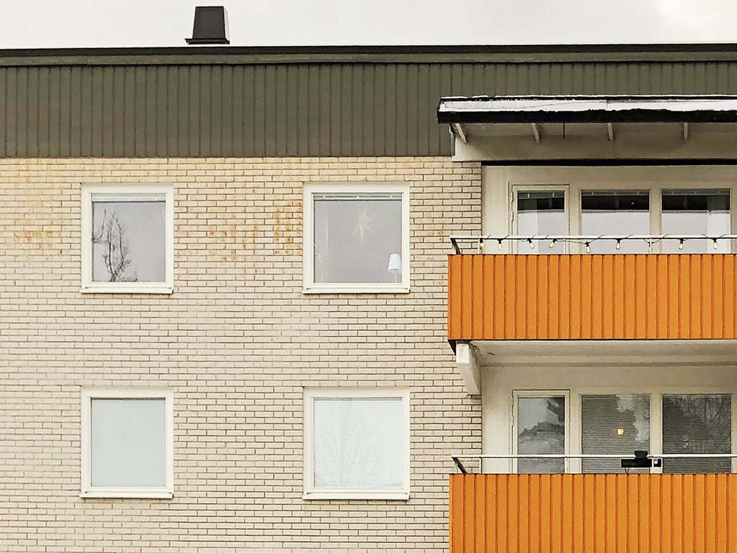 Närbild på nybytta fönster med vita karmar på ljus tegelfasad med orange balkonger – byte av ca 1300 fönster utfört av Mockfjärds.