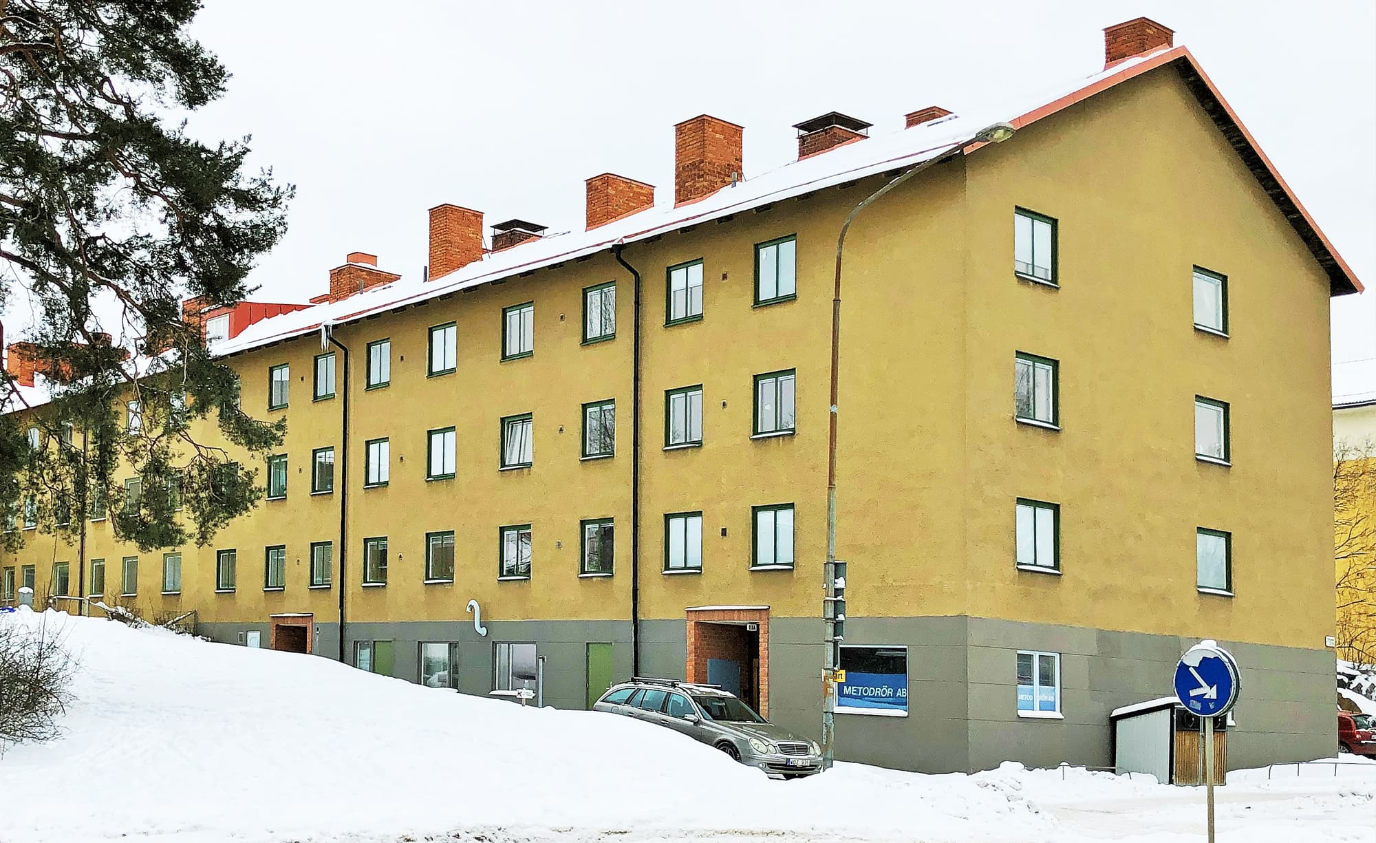 Exteriör av flervåningshus med gul putsfasad och nybytta fönster med gröna karmar – byte av ca 100 fönster utfört av Mockfjärds.