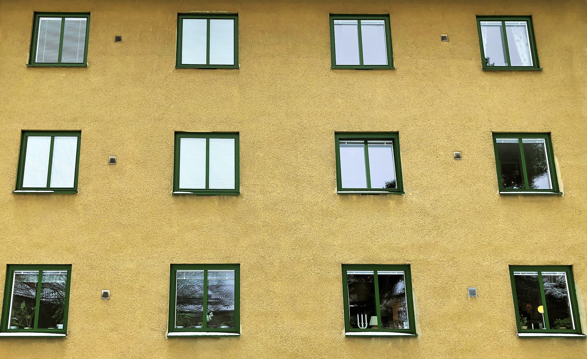 Närbild på nybytta fönster med gröna karmar på gul putsfasad – byte av ca 100 fönster i bostadsrättsförening utfört av Mockfjärds.