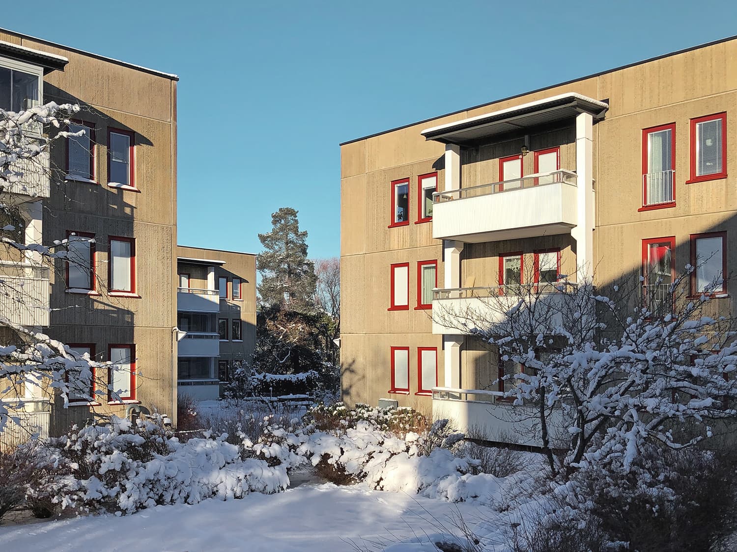 Innergård med flervåningshus och nybytta fönster med röda karmar på beige betongfasad – del av byte av ca 1100 fönster utfört av Mockfjärds.