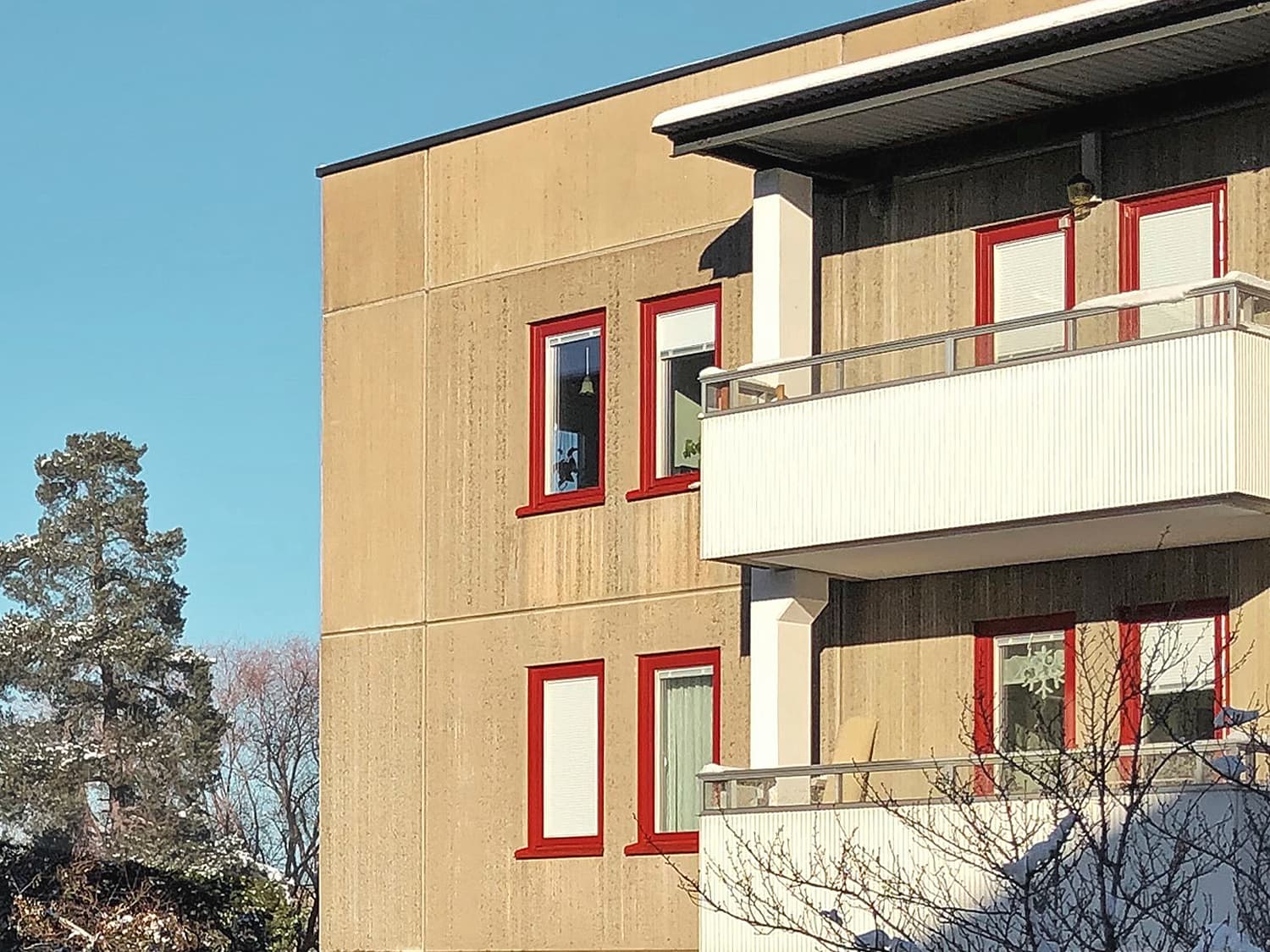 Närbild på nybytta fönster med röda karmar på beige betongfasad med balkonger – storskaligt fönsterbyte av ca 1100 fönster utfört av Mockfjärds.