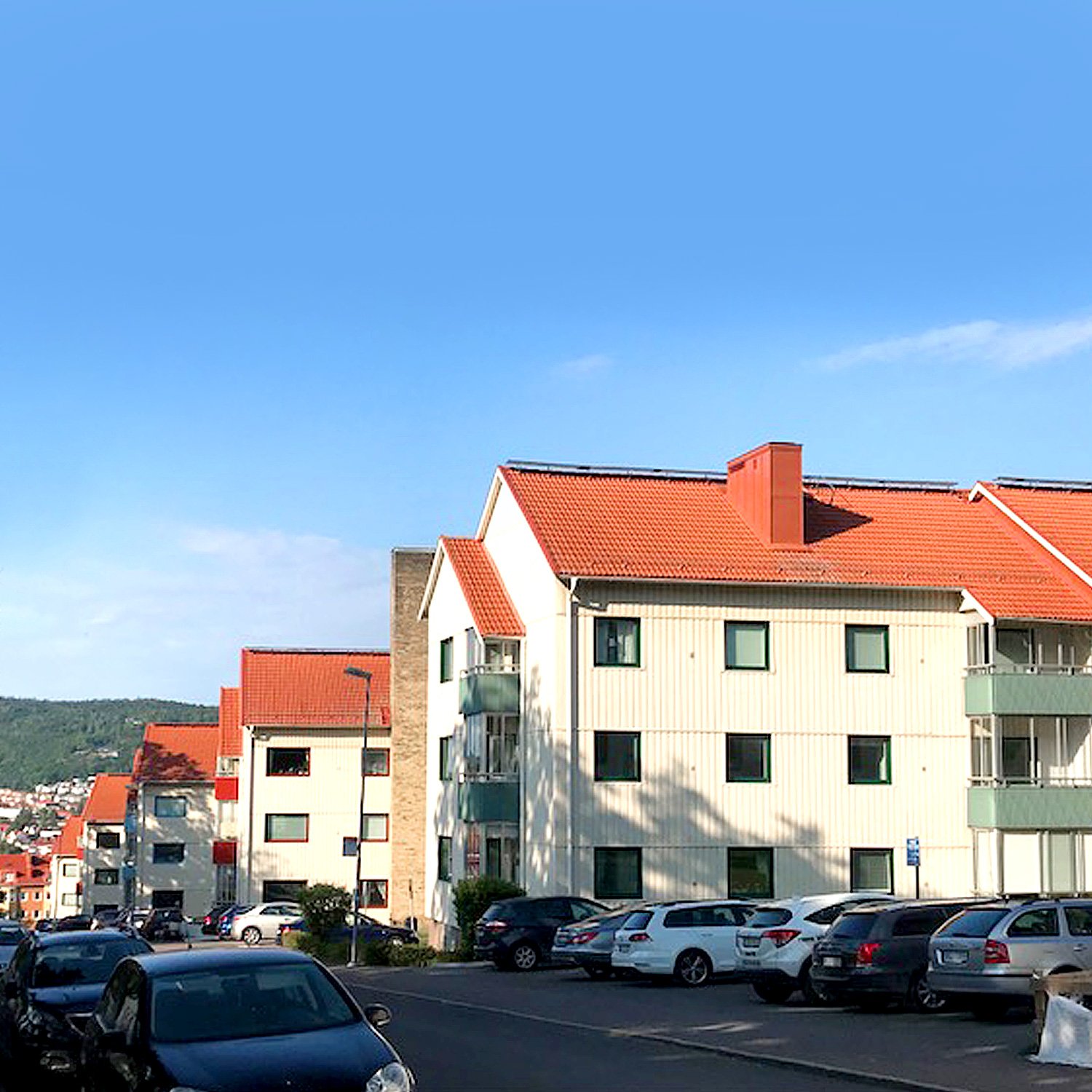 Exteriör av BRF Majstången i Huskvarna med ljus plåtfasad och röda tegeltak – fönsterbyte med måttanpassade vridfönster i åtta fastigheter utfört av Mockfjärds.