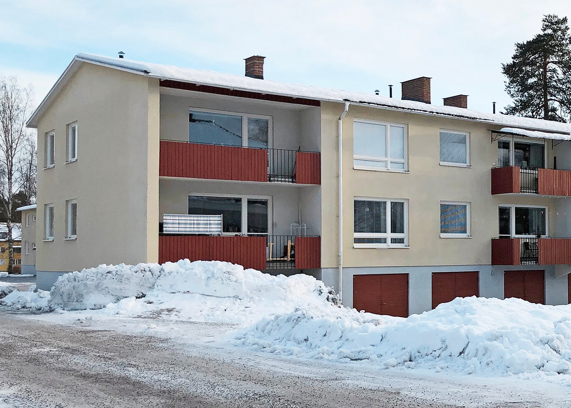 Fönsterbyte i bostadsrättförening – flervåningshus med ljus puts, röda balkonger och nybytta vita fönster. Vintermiljö med snö.