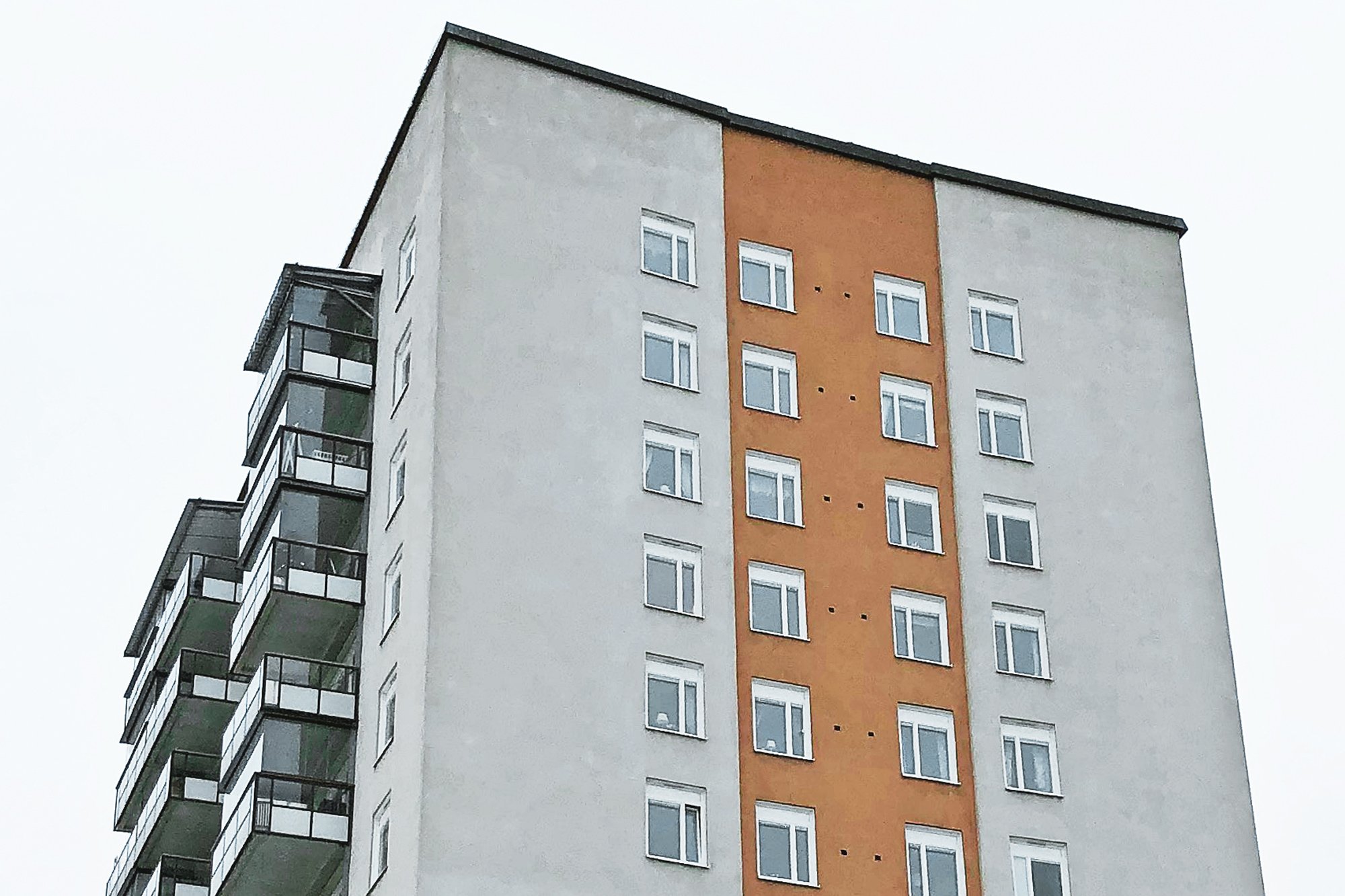 Närbild på höghus med nybytta vita fönster på vit och orange putsfasad – del av byte av ca 900 fönster av Mockfjärds.