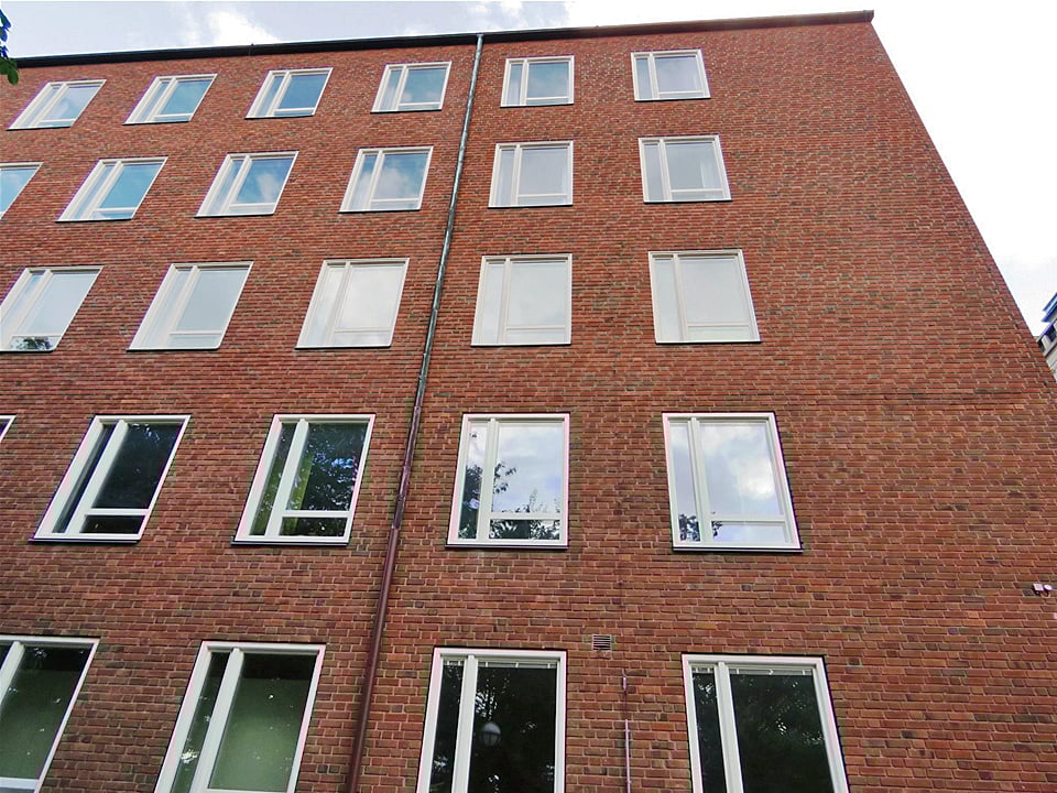 Fasadvy av flervåningshus i rött tegel med nybytta fönster med vita karmar – byte av 287 fönster med nya stuprör och fönsterbleck i Reinzink, utfört av Mockfjärds.