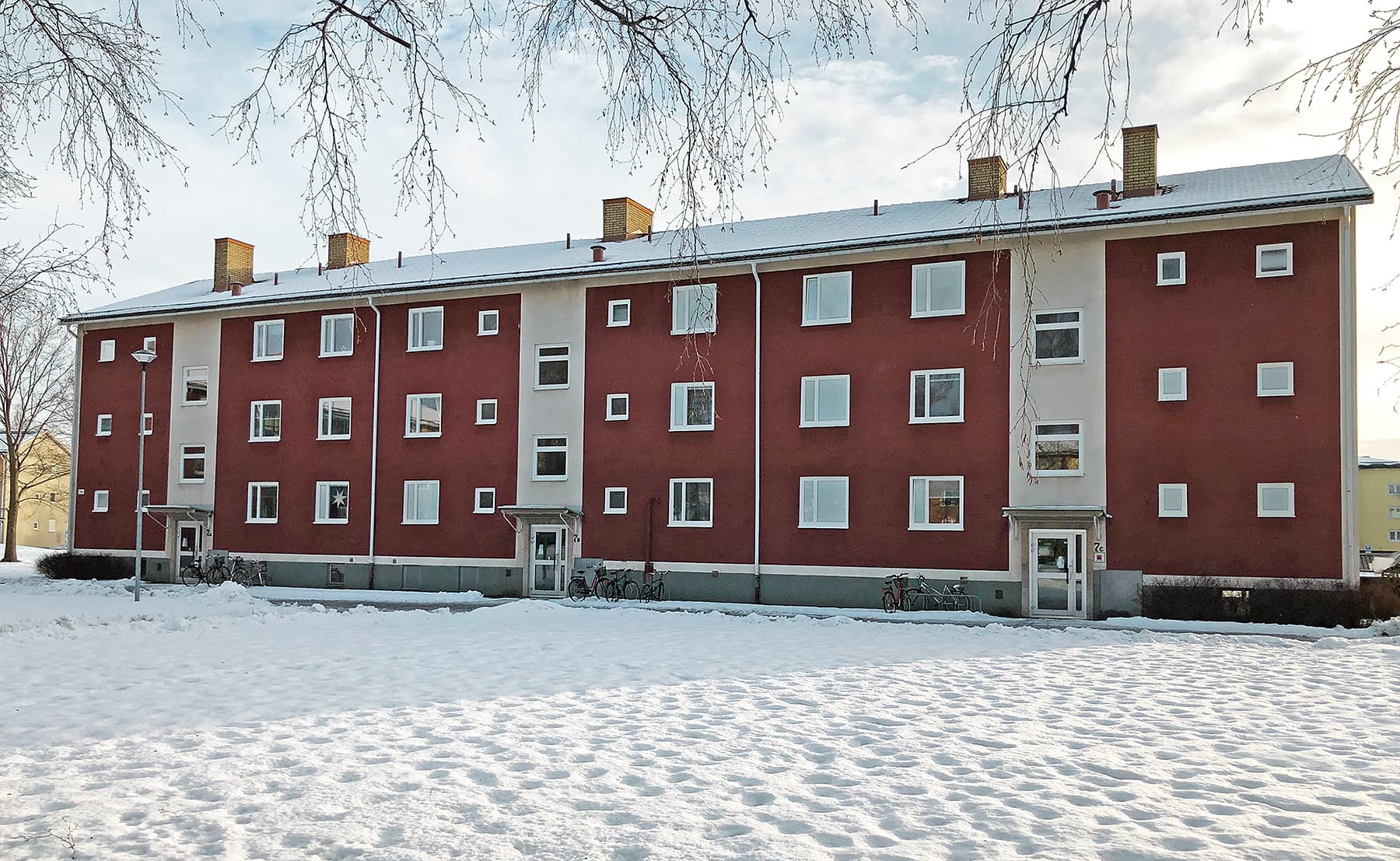 Exteriör av kommunalt flervåningshus med röd putsfasad och nybytta fönster med vita karmar – byte av ca 350 fönster utfört av Mockfjärds.