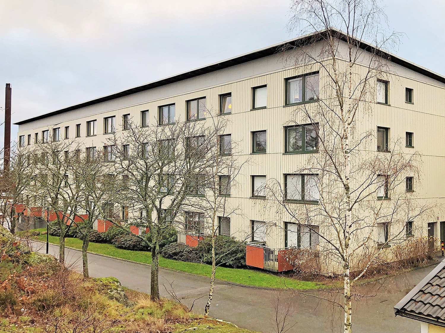 Exteriör av stort flervåningshus med ljus träpanelfasad och nybytta fönster med mörka karmar – byte av ca 600 fönster och entréportar av Mockfjärds.