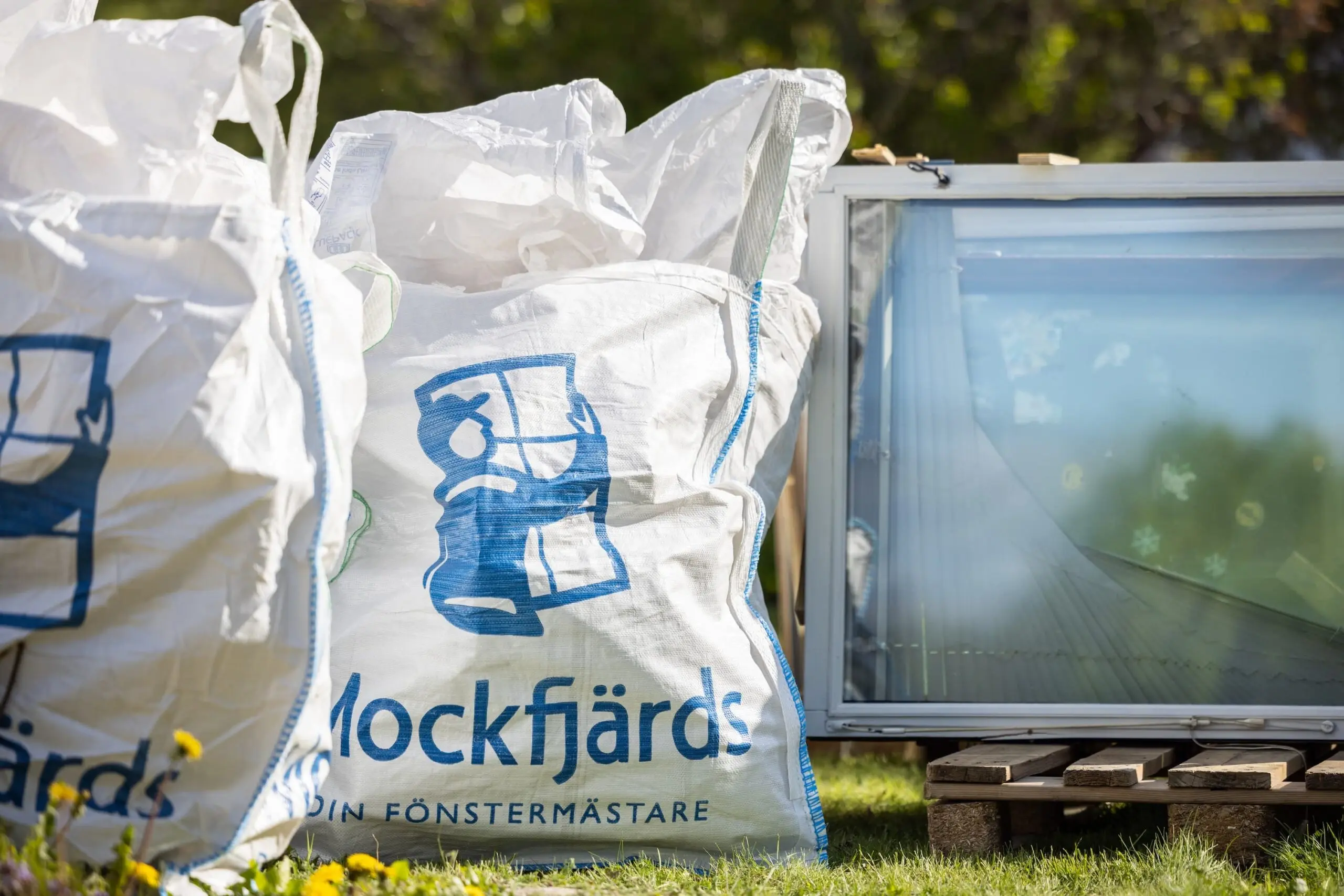 Vita big bags med Mockfjärds logotyp fyllda med uttjänta fönster redo för återvinning utanför villa i Sundsvall, med ett gammalt fönster stående bredvid.