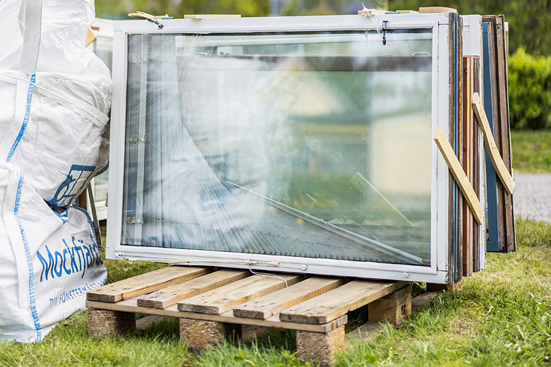 Gamla fönster staplade på pall för återbruk eller återvinning.