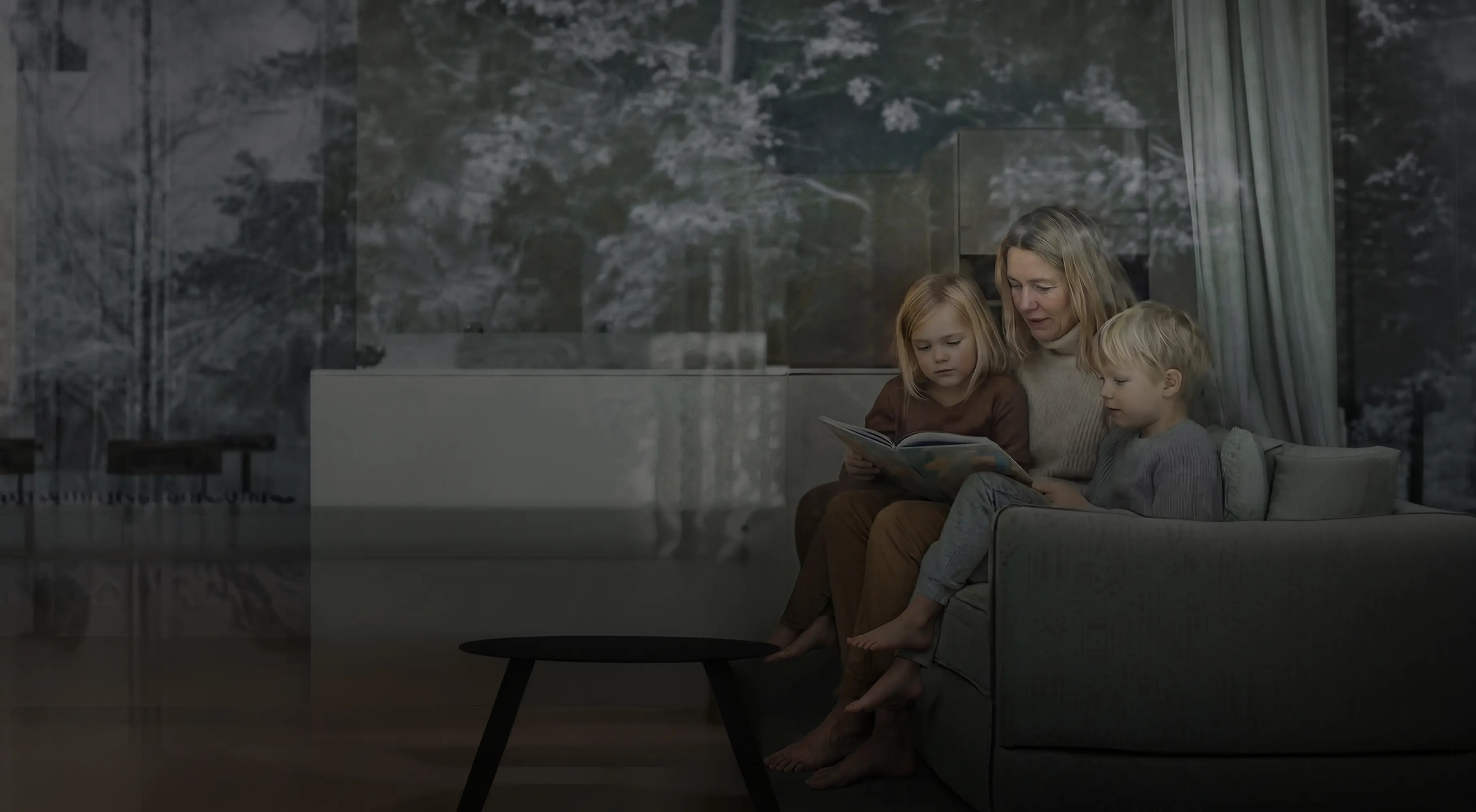 Kvinna och två barn sitter vid ett fönster och ser ut, med träd reflekterade i glaset.