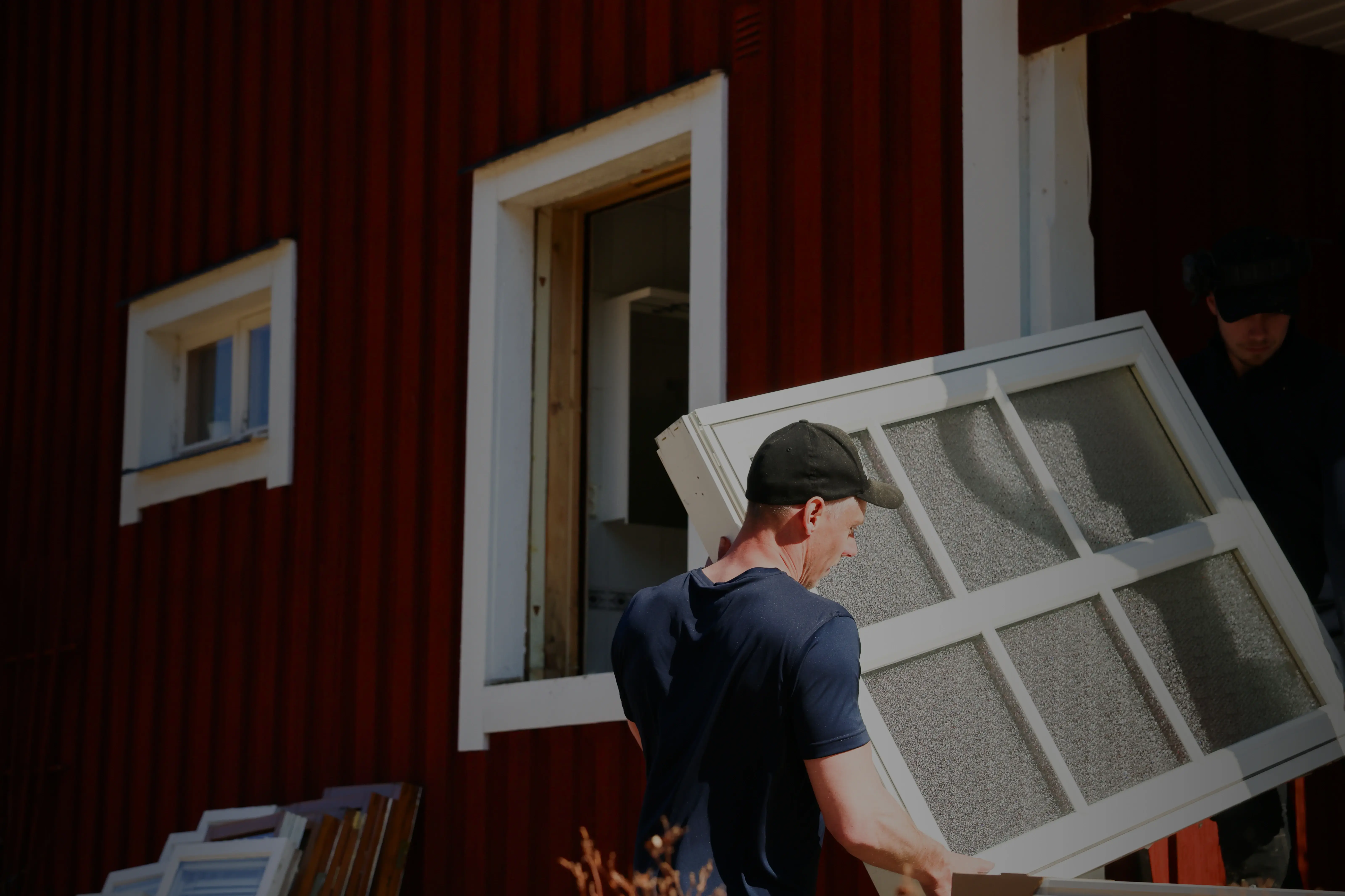 Montör bär in ett nytt fönster i ett rött hus med vita knutar