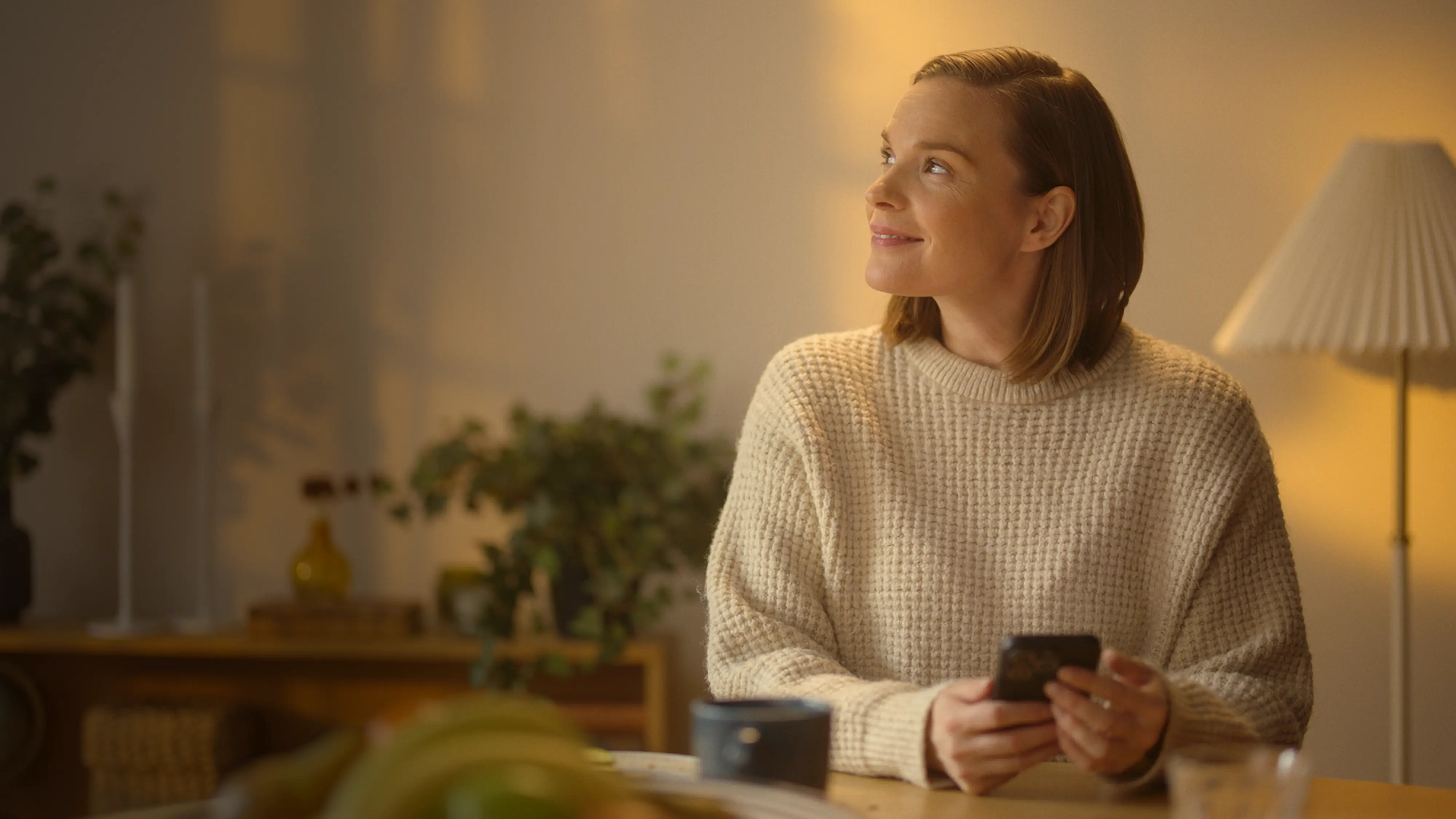 Kvinna i kvällssol inomhus håller i en telefon och ler