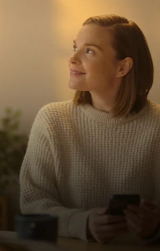 Kvinna i kvällssol inomhus håller i en telefon och ler