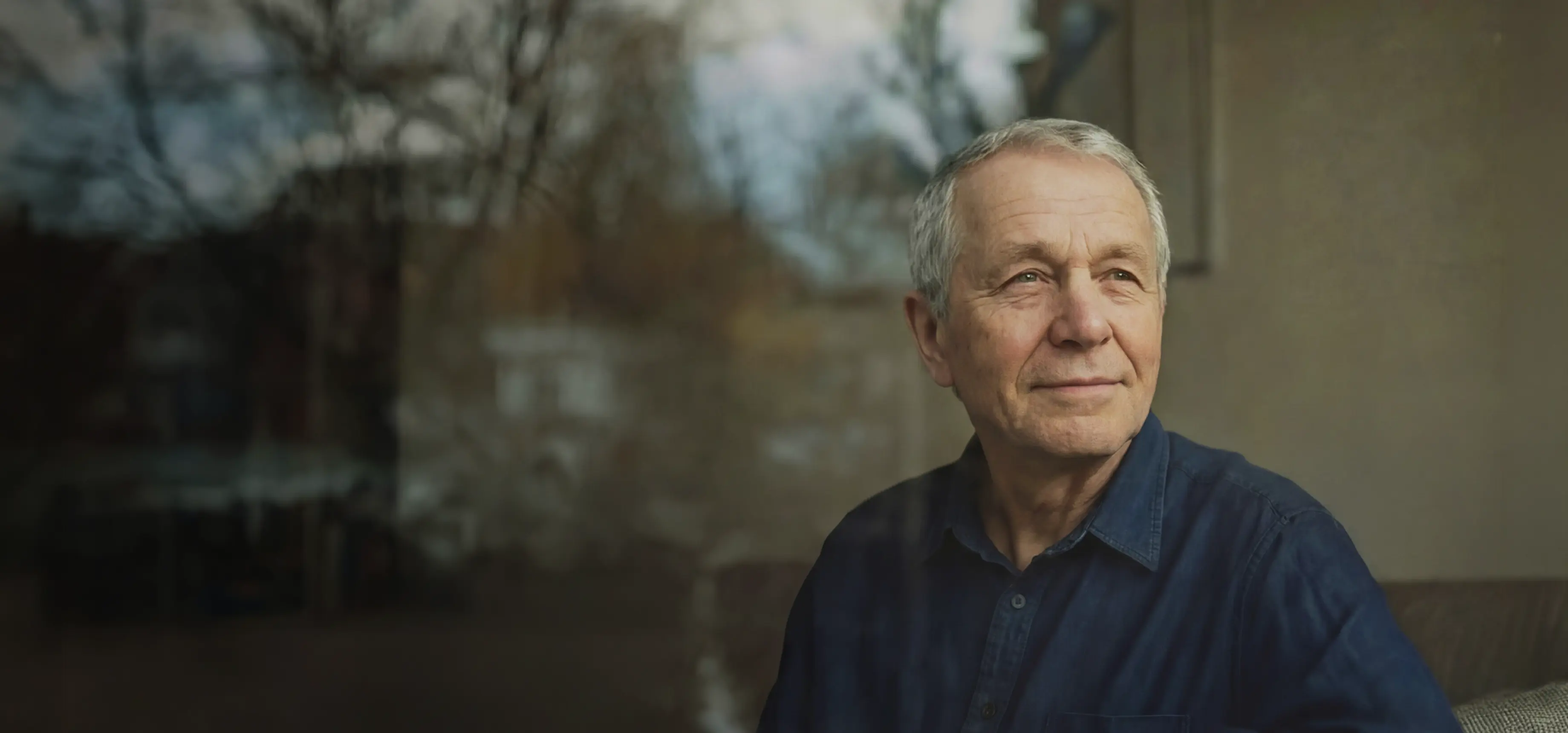 Äldre man sitter vid ett fönster och ser ut genom glaset.