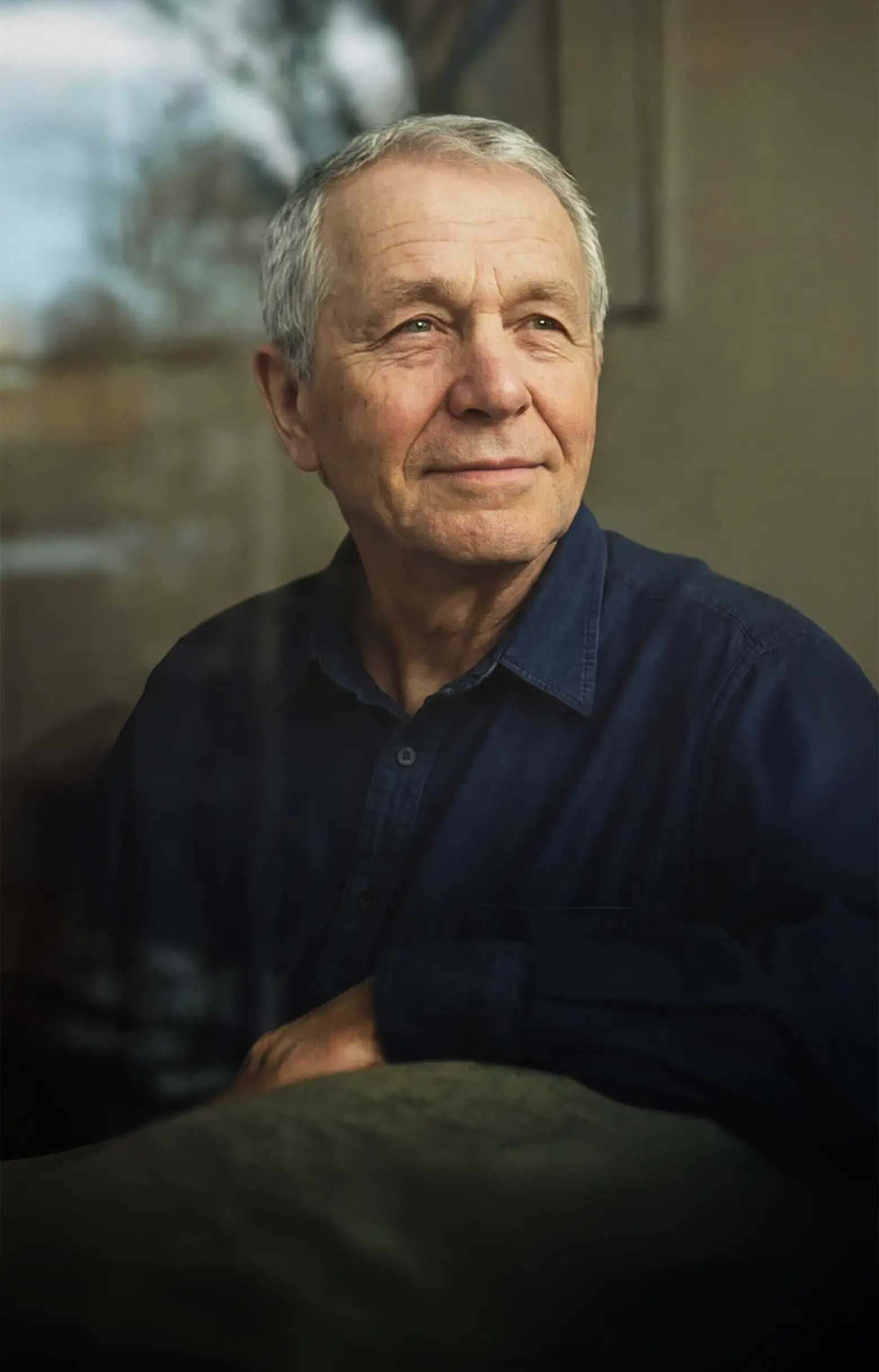 Äldre man sitter vid ett fönster och ser ut genom glaset.