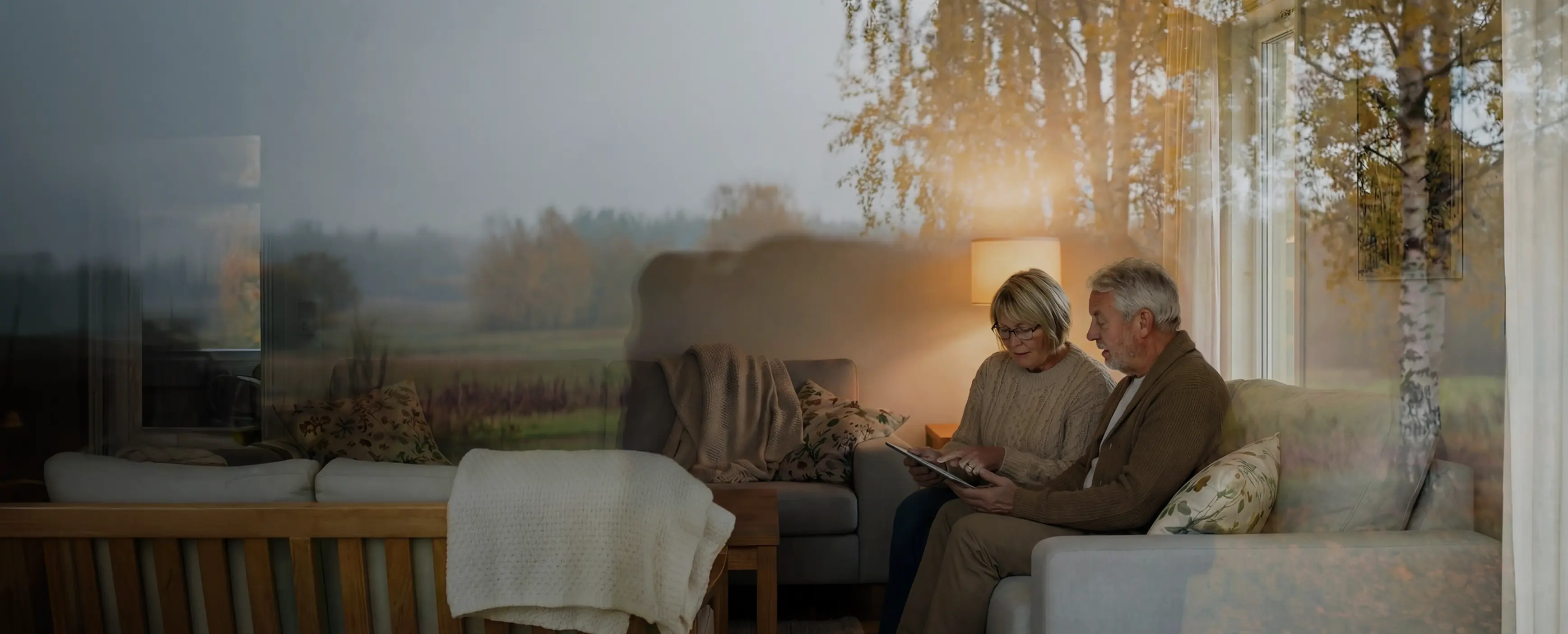 Äldre par sitter i en soffa och scrollar med em iPad i vardagsrummet.