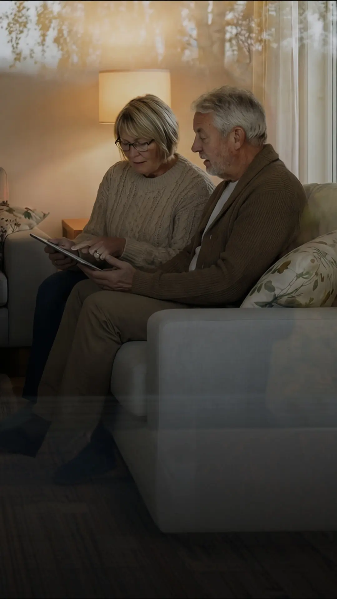 Äldre par sitter i en soffa och scrollar med em iPad i vardagsrummet.