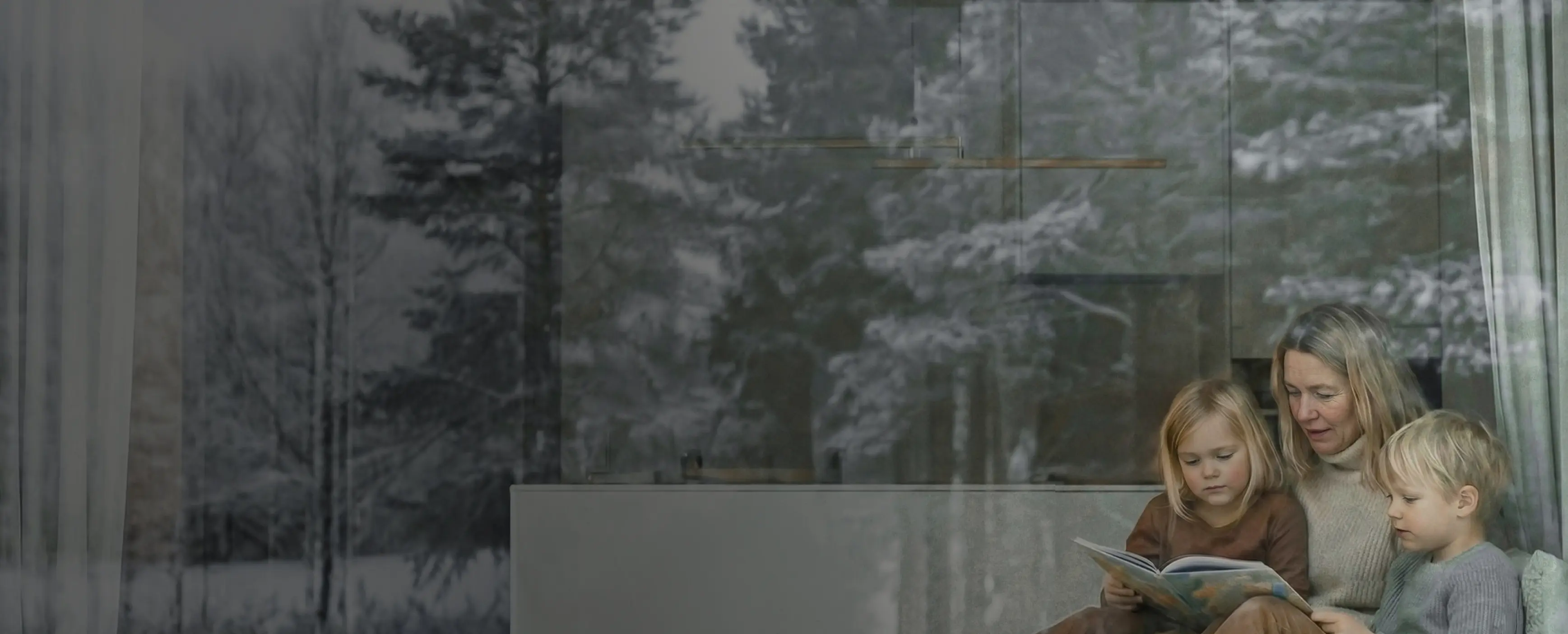 Kvinna och två barn sitter vid ett fönster och ser ut, med träd reflekterade i glaset.