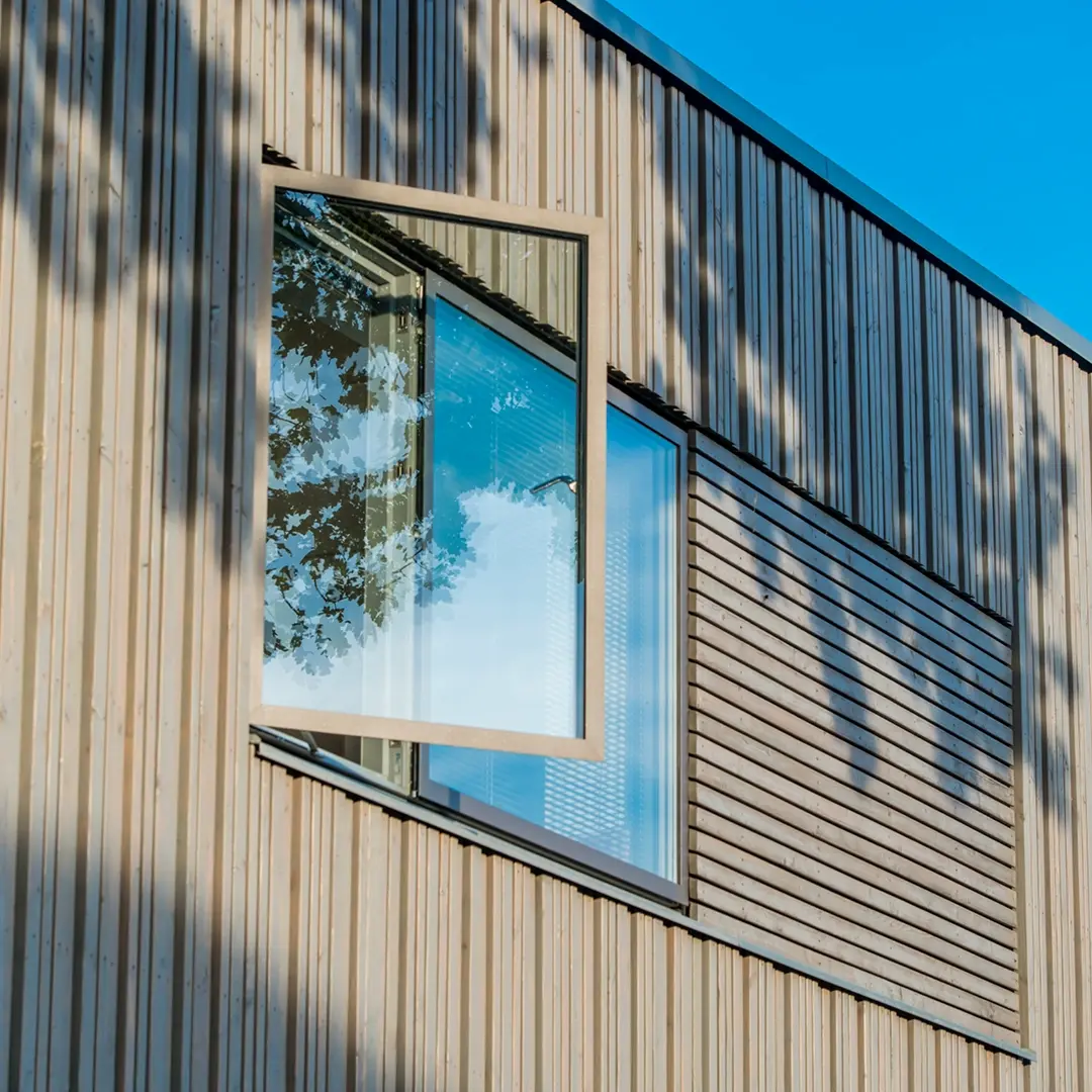 Öppet fönster på en modern träfasad med reflektion av träd och himmel i glaset.